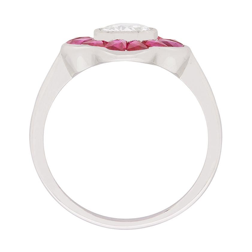 This unusual ring features a centre rub over diamond weighing 0.70 carat. It has been graded as a H in colour and SI1 in clarity and is haloed by french cut rubies. The rubies have a pink hue which makes them sparkle and they have been cut to fit