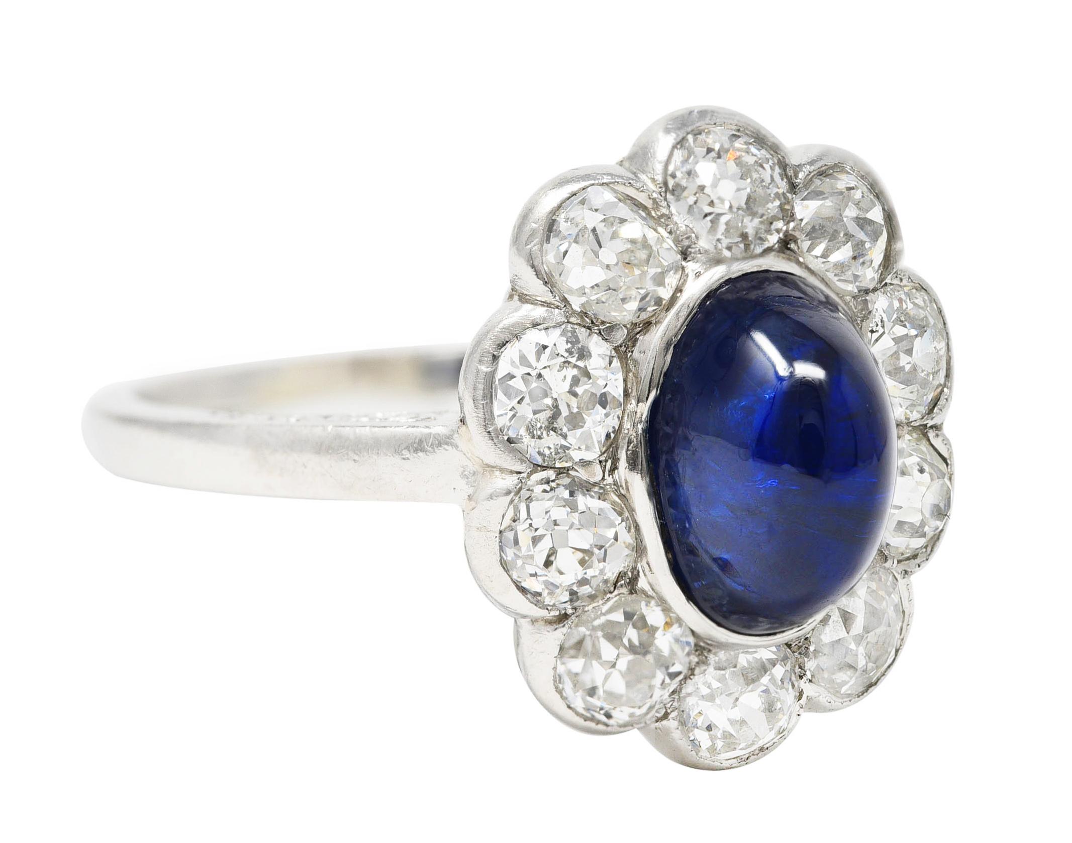 Centering an oval shaped sapphire sugarloaf cabochon weighing approximately 3.30 carats total. Semi-transparent medium/dark blue in color - bezel set with scalloped halo surround. Featuring old European cut diamonds weighing approximately 1.60