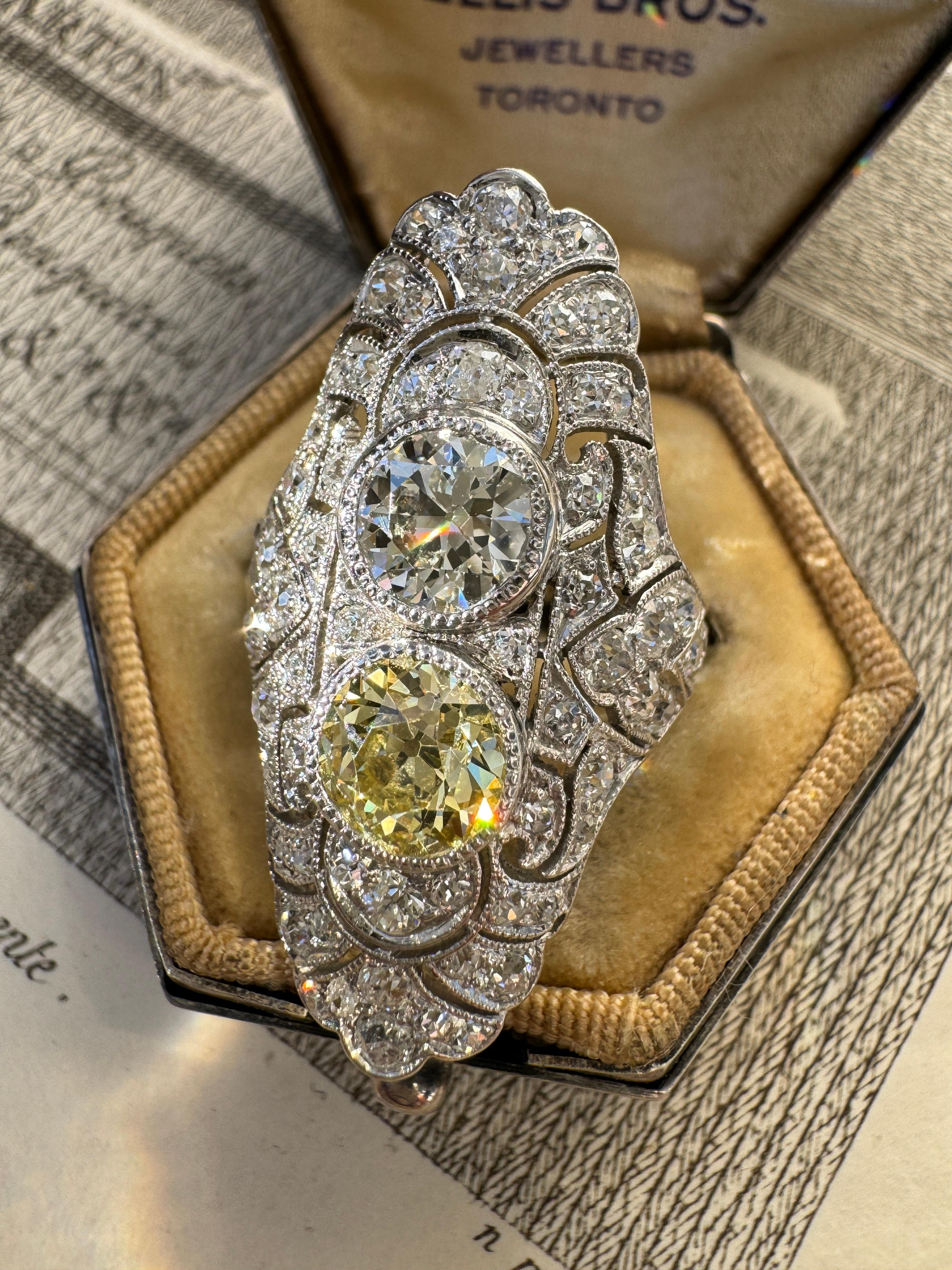 Intricately hand fabricated in platinum around the first or second decade of the twentieth century, this romantic toi et moi ring centers on a blazing fancy yellow old mine-cut diamond, (GIA 1.24 carats with VS2 clarity), and a dazzling 1 carat old