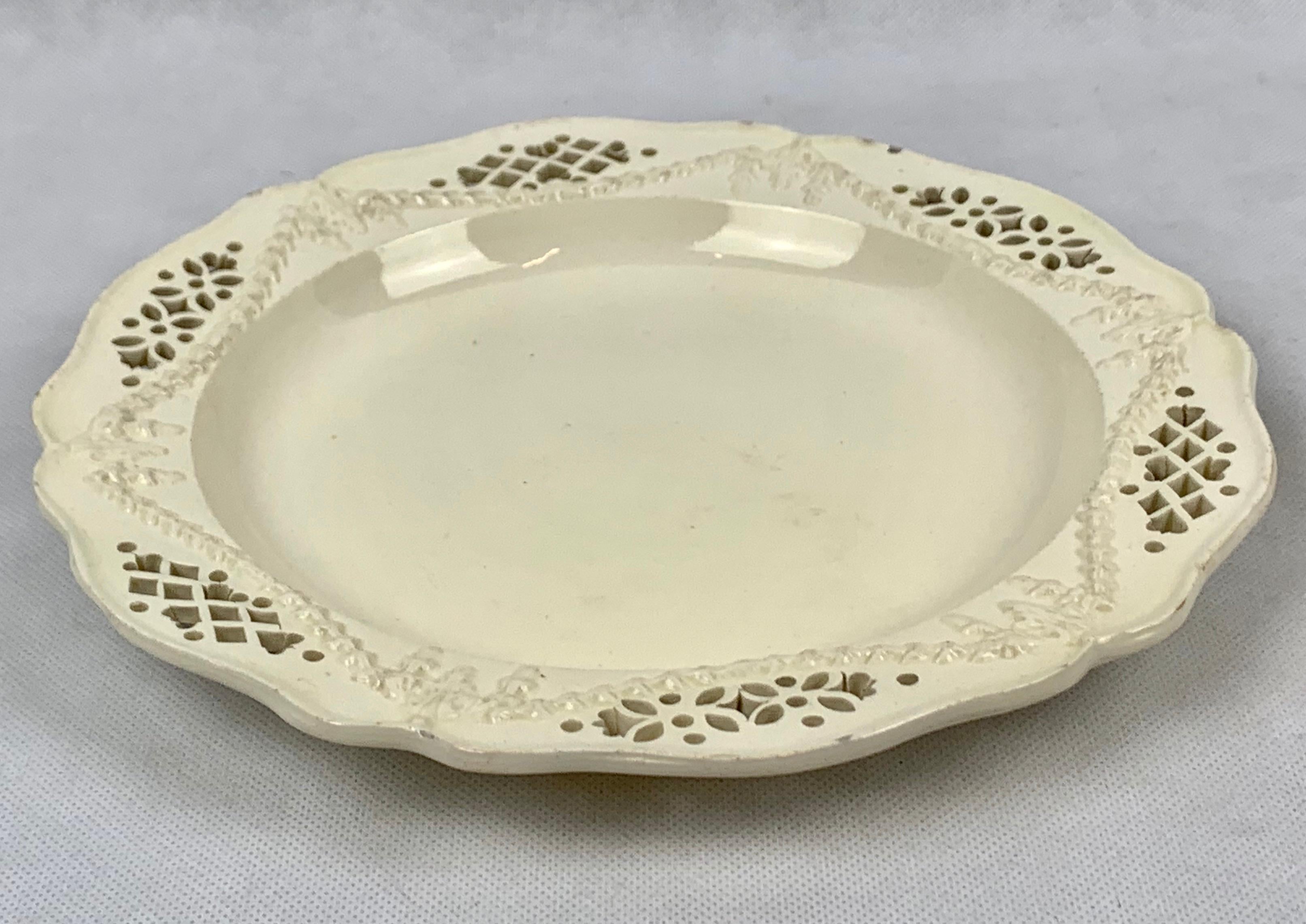 Late 18th century English creamware plate. The scalloped plate edge conforms to a reticulated border with swags of bell flowers. The center of the plate has a deep dished out form. There are tiny flakes at the plates edge which are not unusual for a