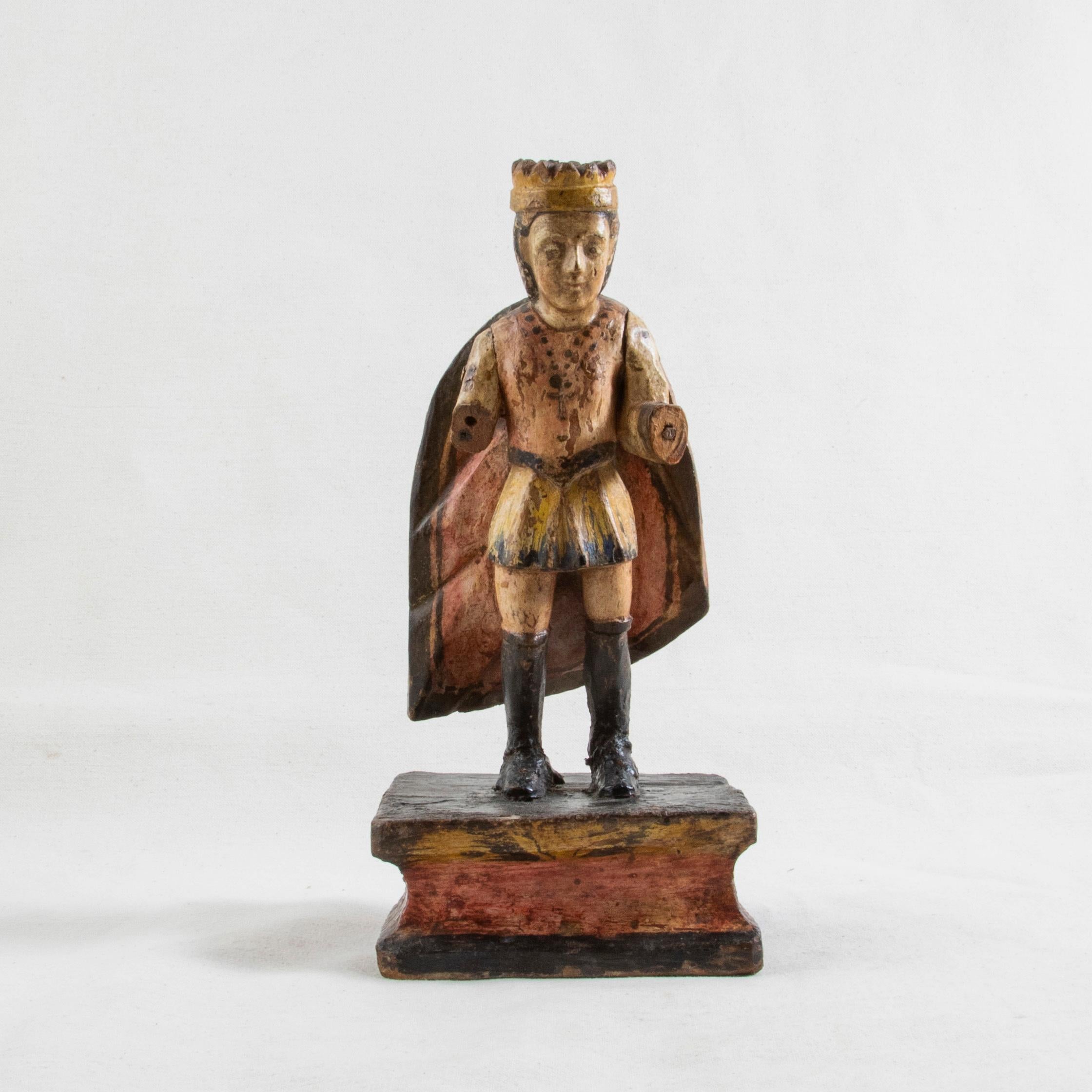 This late 18th century hand carved polychrome sculpture from Spain features the figure of a king wearing a crown and cape. The king stands in knee high boots and wears a short tunic and a cross hanging from a chain around his neck. His arms are hand