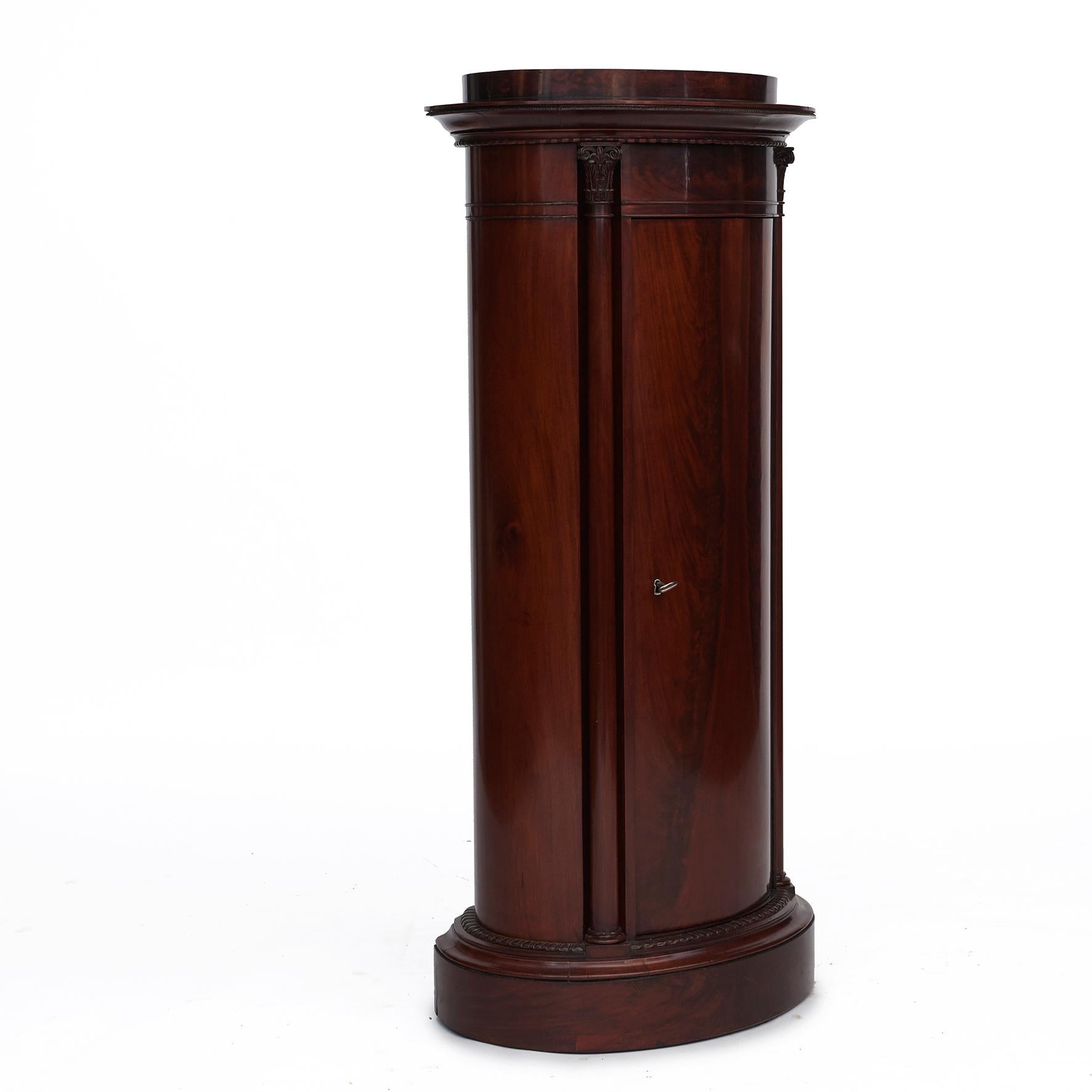 Oval pedestal cabinet, late empire.
Mirror-cut flamed mahogany with beautiful grain. Door flanked by columns with wood-carved capitals.
Behind the door 3 shelves.

Gently French repolished in perfect condition.
Includes original