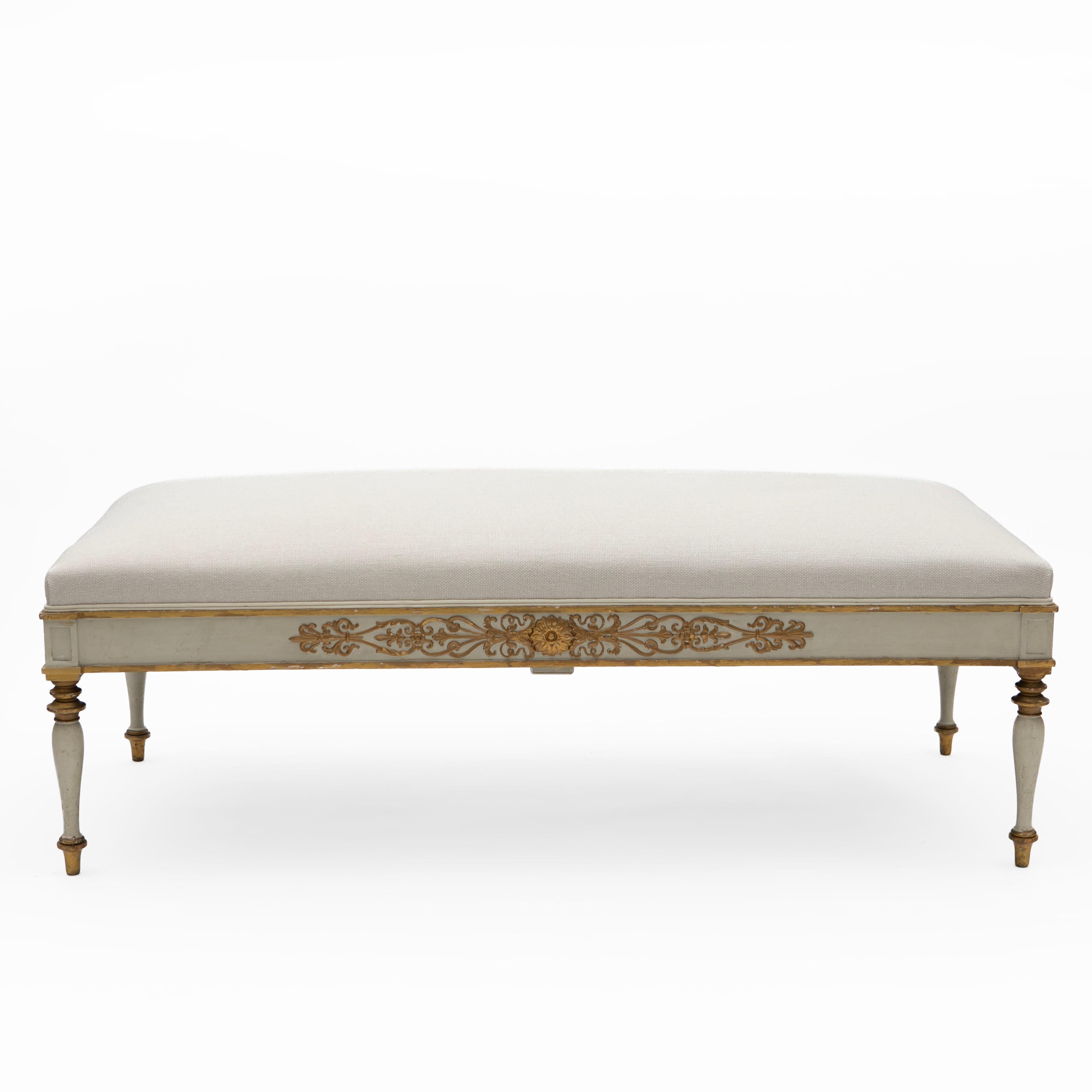 Decorative and elegant Late Empire bench with upholstered seat.
Frame crafted in beech with original white color and delicate gilt wood carved details.
Resting on elegant turned tapered legs with gilt details at the top and bottom.
Seat with