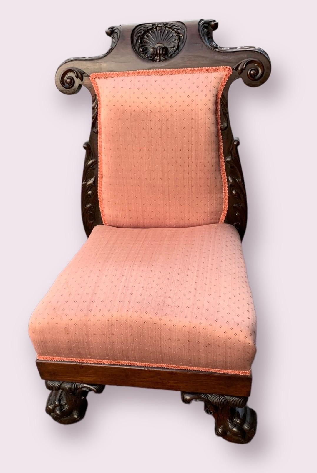 Il s'agit d'une ancienne chaise à pantoufles en forme de prie dieu, datant de la fin du 19e siècle, en noyer sculpté à la main et recouverte d'une tapisserie de couleur corail clair. La coquille sculptée très détaillée sur le cimier constitue une