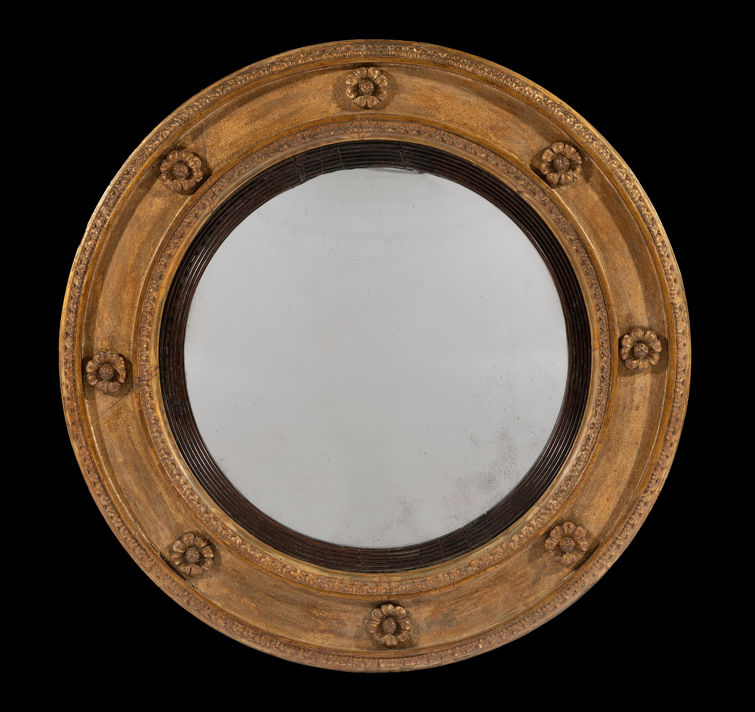 The original glass plate has a shallow convex surmounted on an ebonies reeded slip and sits in a circular giltwood frame. The rosettes are crisply carved and the overall style of the mirror is more late Georgian than the 'Regency' convex frames that