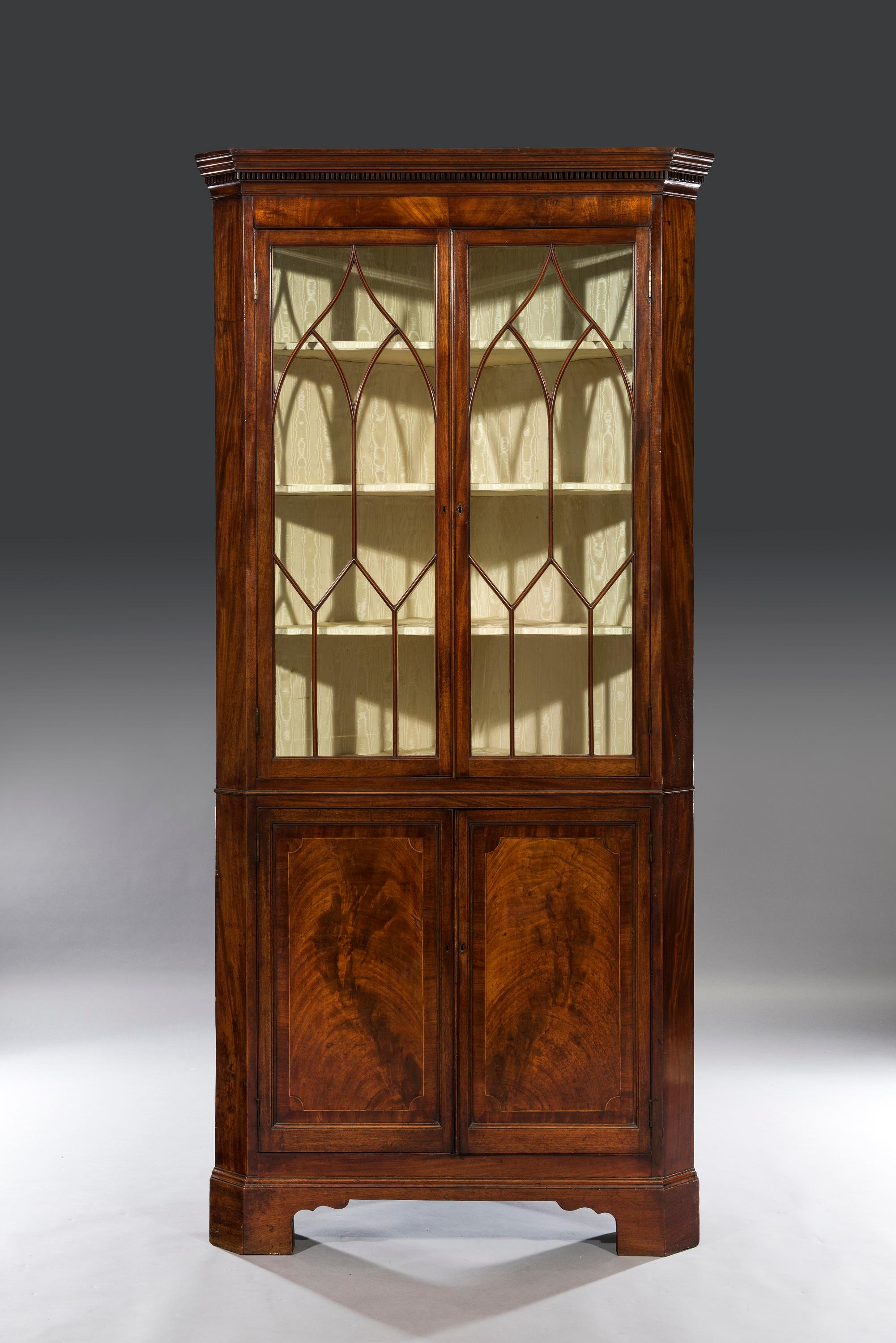 The standing corner cupboard is of impressive size and comes in one piece. The fitted moulded top with a dog-tooth dental moulding sits above a flamed veneered frieze and astragal glazed doors which open to silk lined fitted shelves.  The glazed top