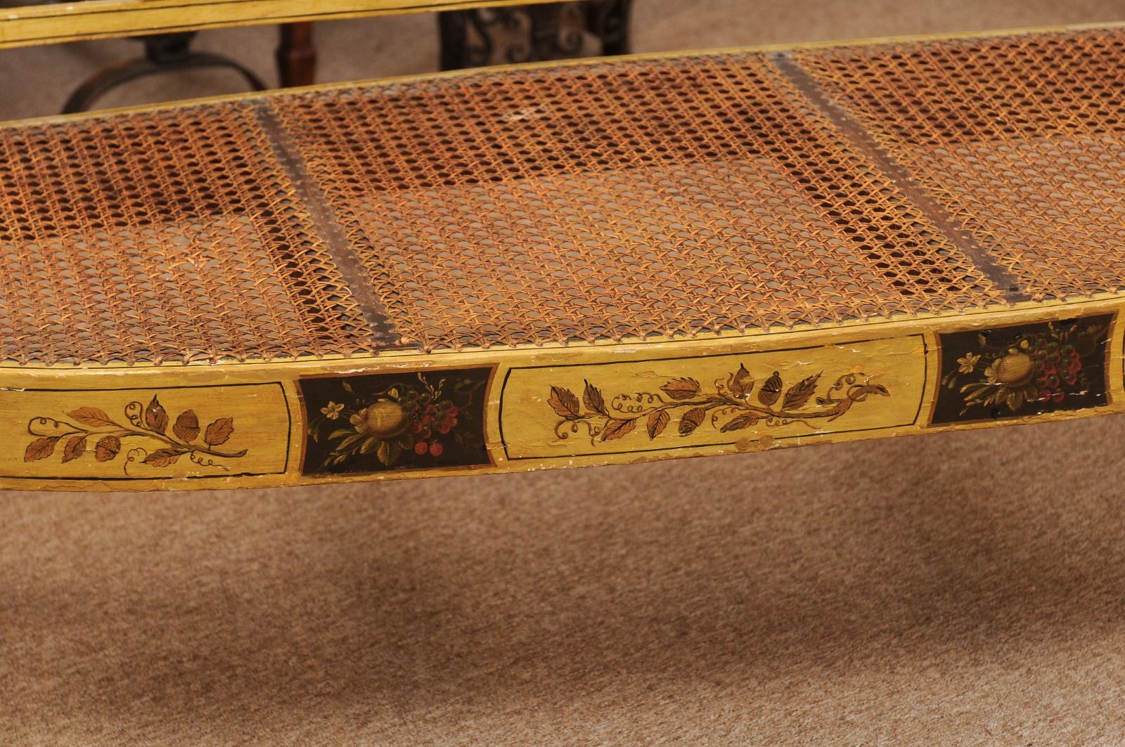 An early 19th century late George III English ochre painted settee with painted foliage and flower detail and caned seat.