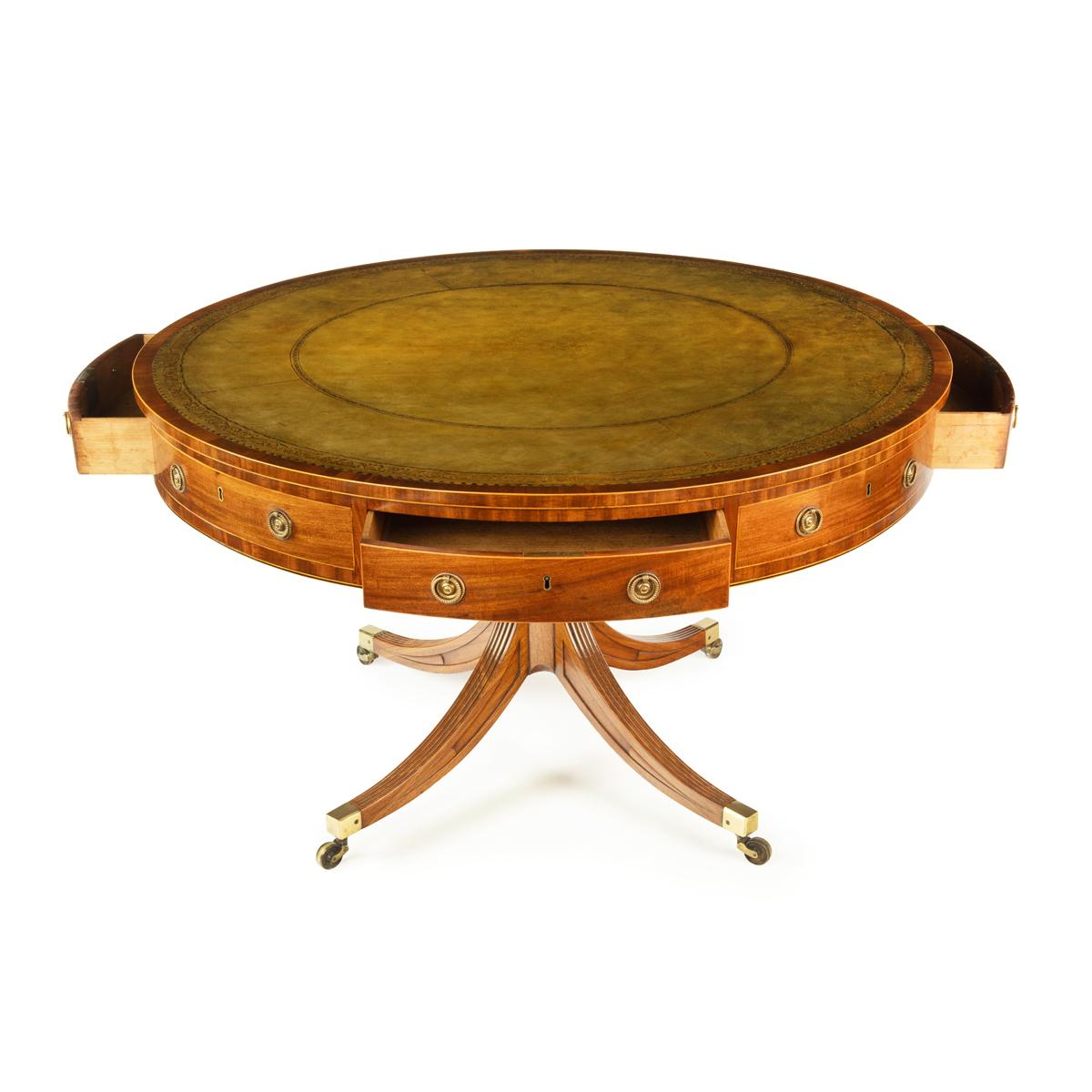 A late George III revolving mahogany drum table attributed to Gillows, the circular top inset with a faded and gilt tooled green leather above four full and four dummy frieze drawers, raised on a turned and gadrooned support with four reeded and