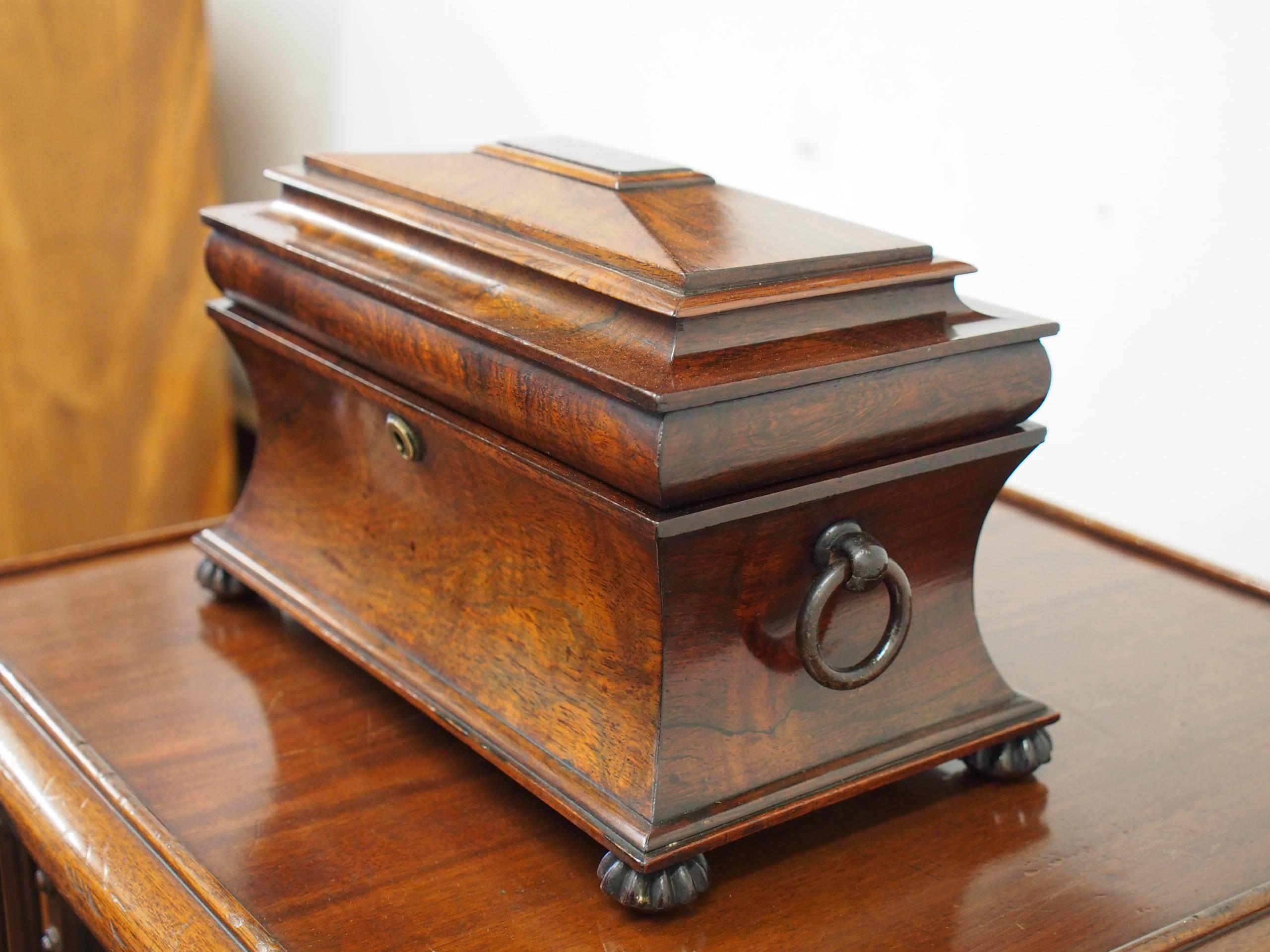 Late George IV rosewood sarcophagus shape tea caddy, circa 1830. It has a shaped top with various mouldings, and opens to reveal a pair of hinged containers either side of a circular aperture (originally for a mixing bowl). The inside of the lid is