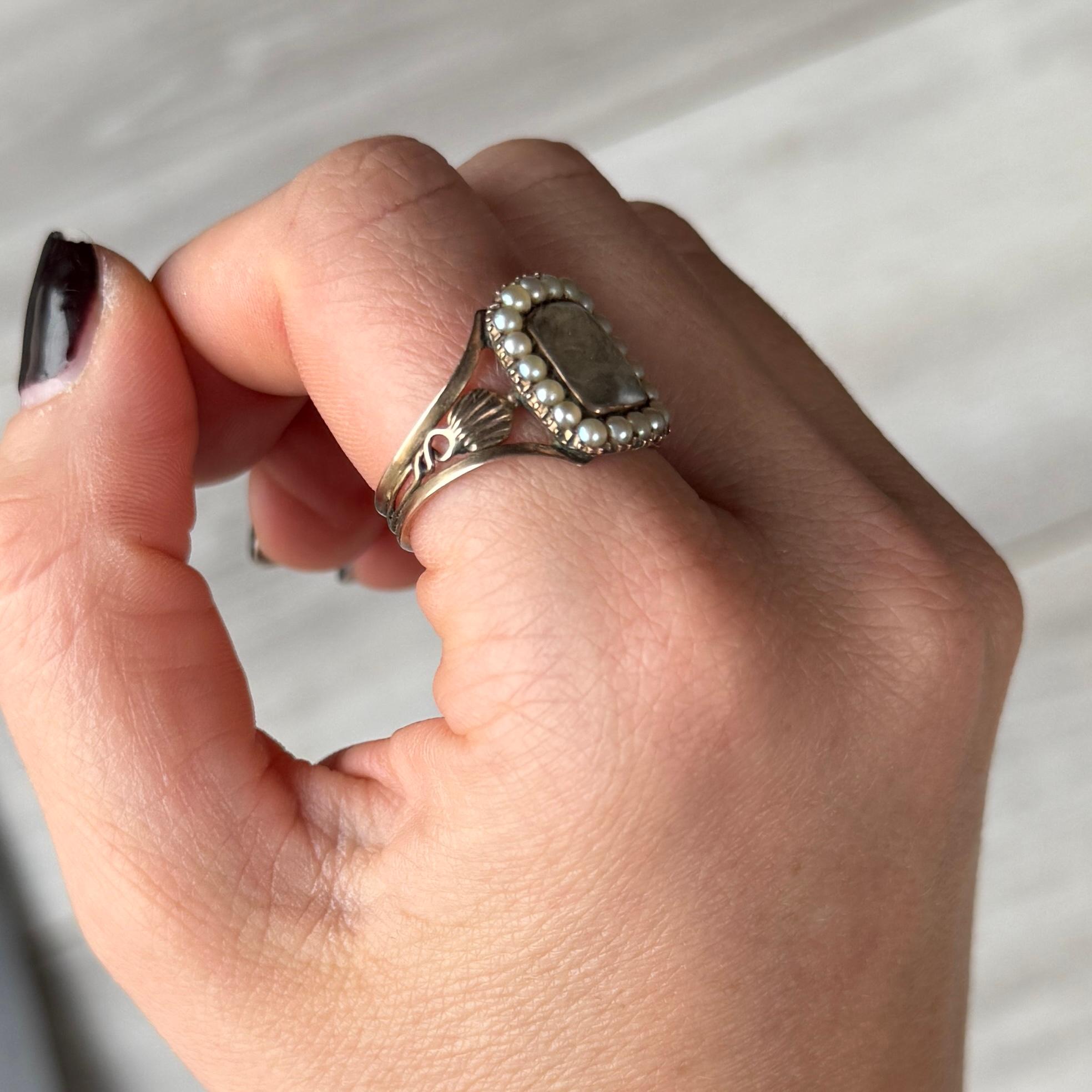 This Georgian ring holds a lock of hair behind glazing. The shoulders of the ring are delicate and decorative. Behind the face of the ring is the inscription 'John Greenslade Ob 28 Ap 1811 at 64'. modelled in 9 carat gold. 

Ring Size: S 1/2 or 9