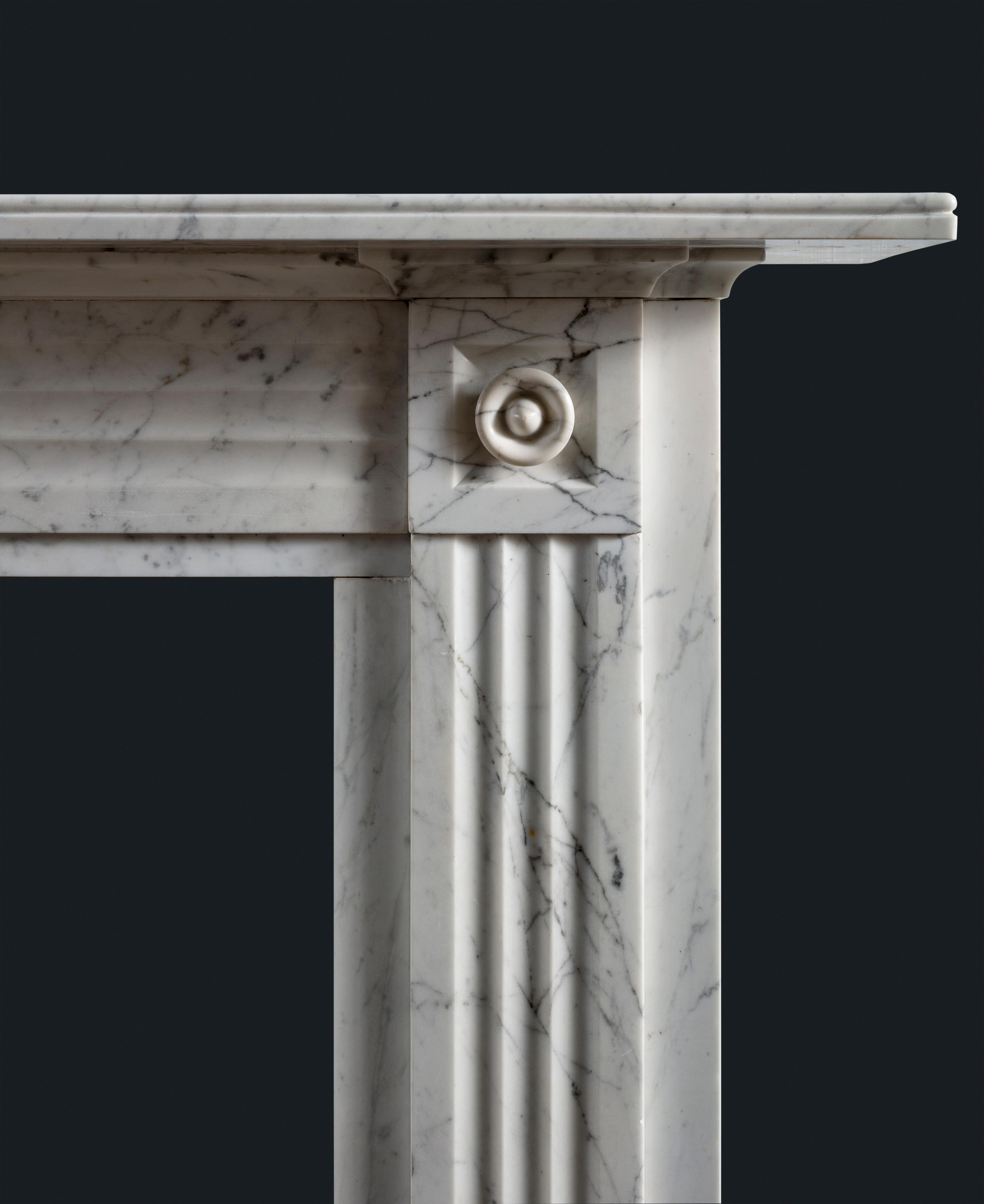 A handsome late Georgian or Regency period fireplace surround carved in delicate and lightly veined pencil veined Statuary marble, its shelf with bead mould above frieze and jambs composed of crisply executed fluted panels, the corner blocks with