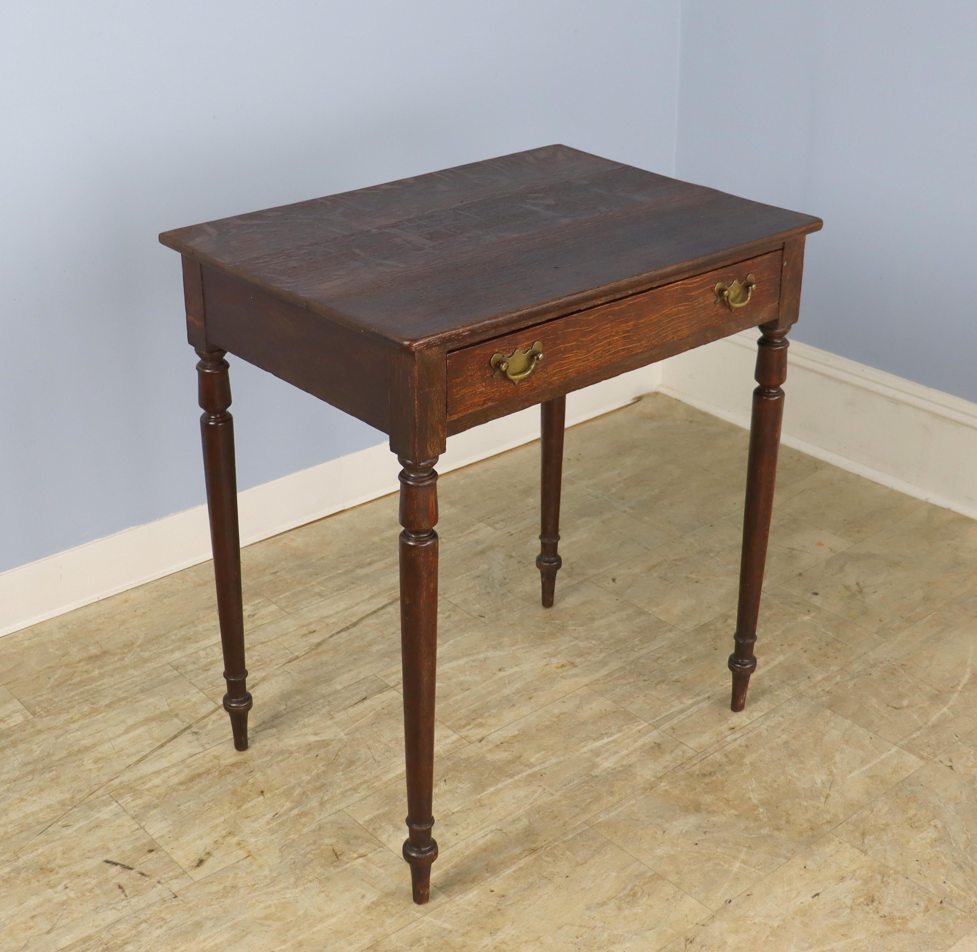 An elegant dark oak side table with slim turned legs and a single roomy drawer. Brasses are original.