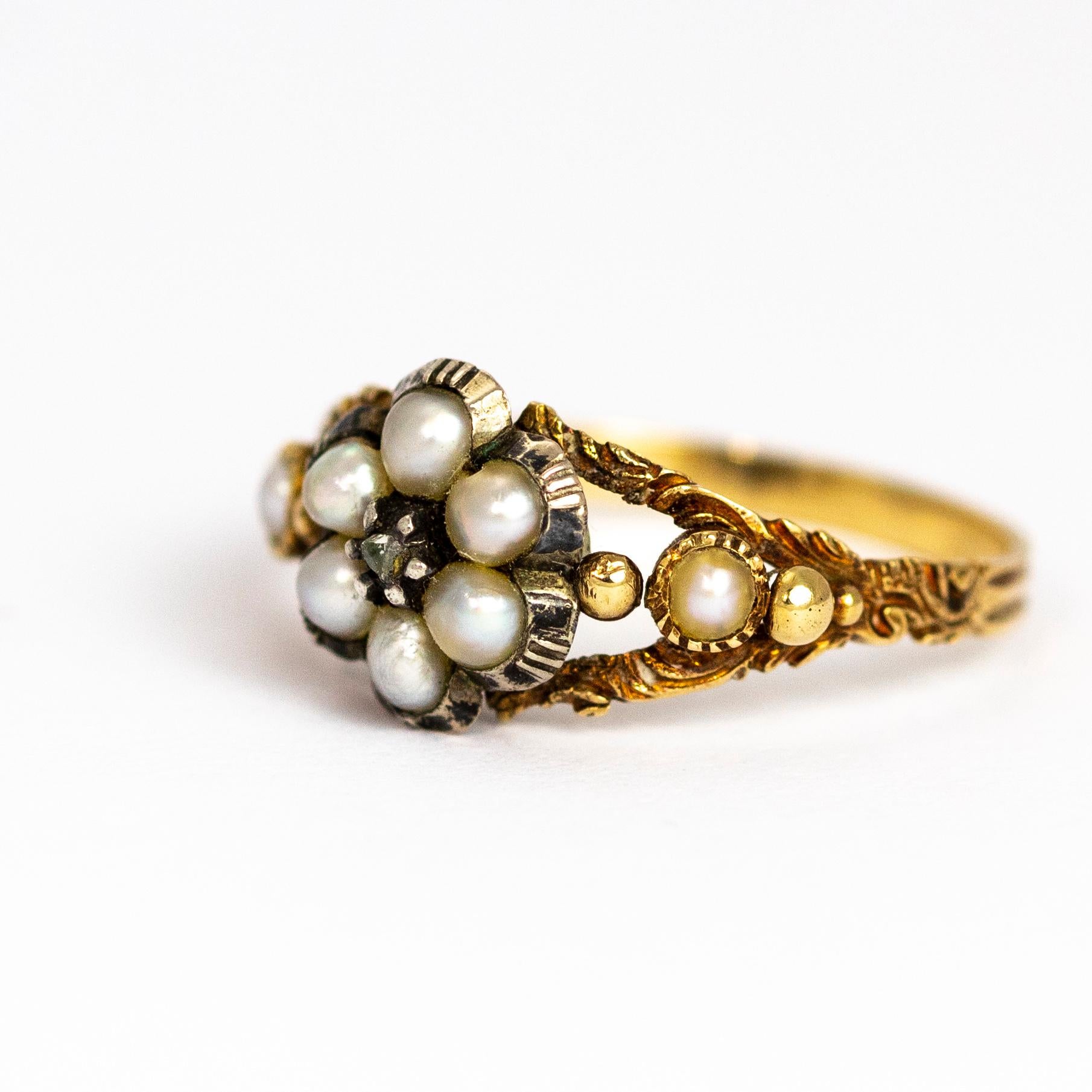 This late Georgian ring holds a rose cut diamond at the centre of the cluster and is surrounded by six pearls. The shoulders of the ring feature a pearl on each and these are also beautifully engraved. Behind the cluster detail is a sweet glazed