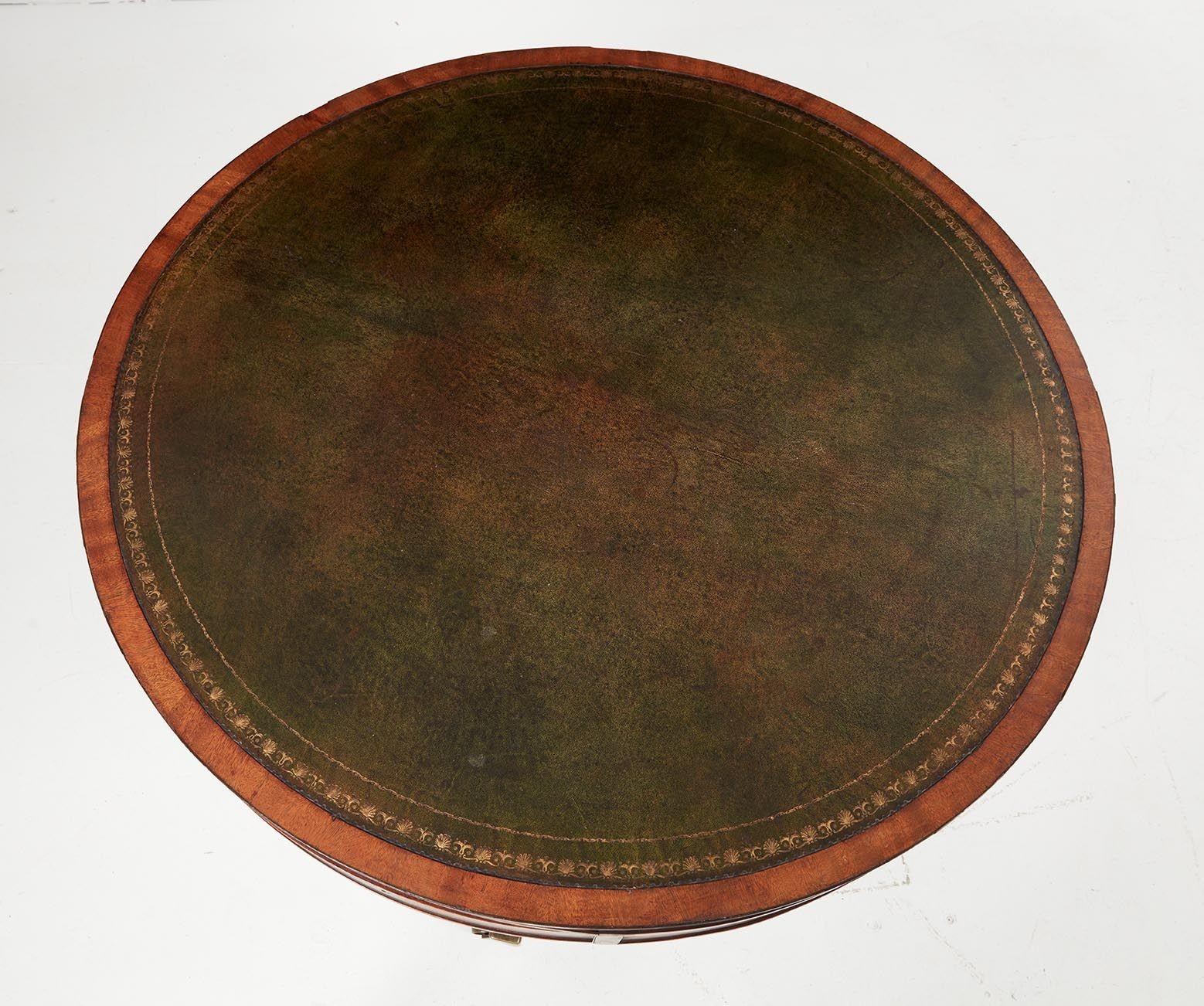 A late Georgian circular mahogany drum table having a leather inset top with tooled and gilt edge on a pedestal with ring turned column stem on three sabered and reed-carved legs ending in brass toe caps and castors. Four drawers, including divided