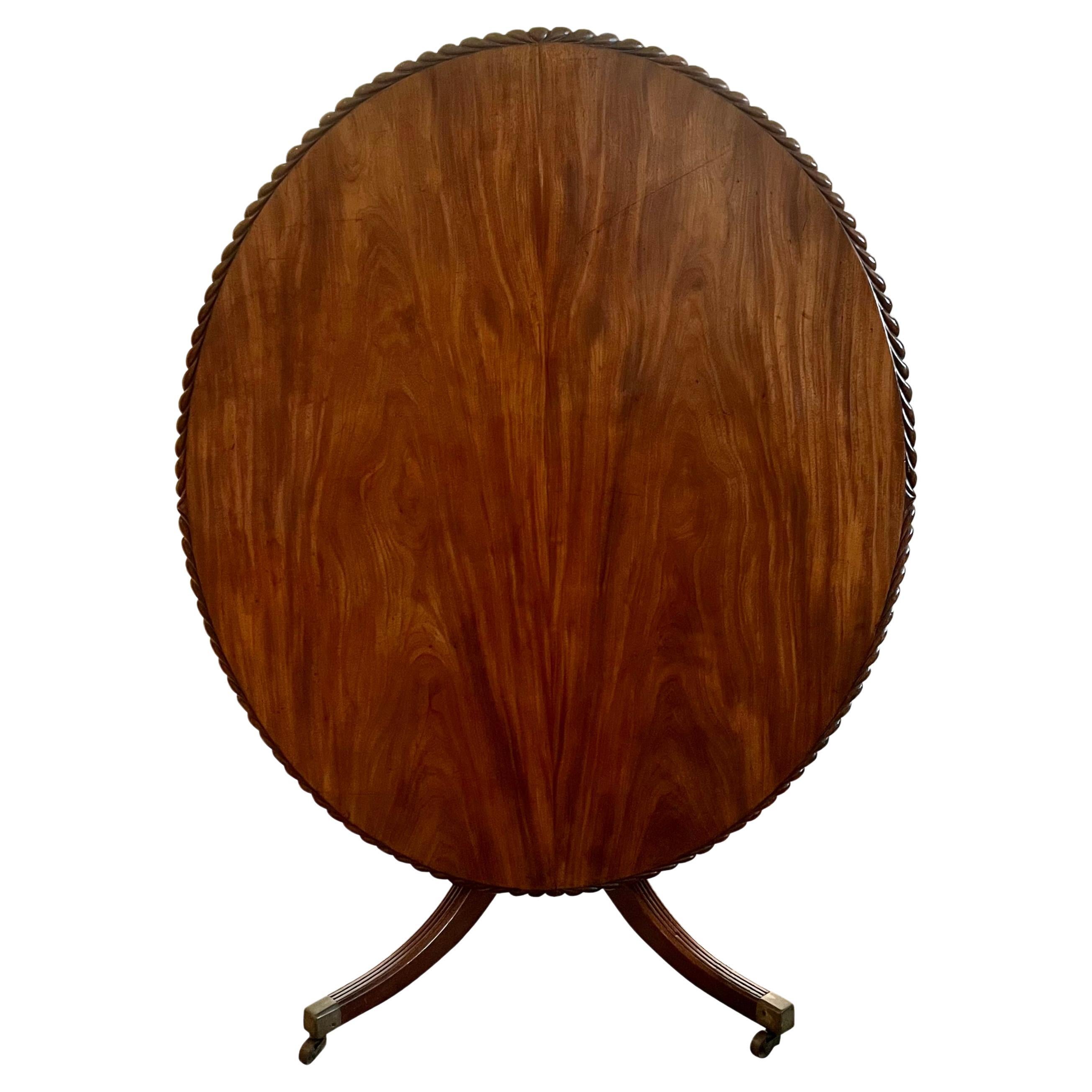 An English late Georgian tilt-top breakfast table, the solid well-figured mahogany top with a bold rope carved edge resting on a quadripartite reeded base ending brass caps on casters. This piece has lovely figuring to the top and a pleasing mellow