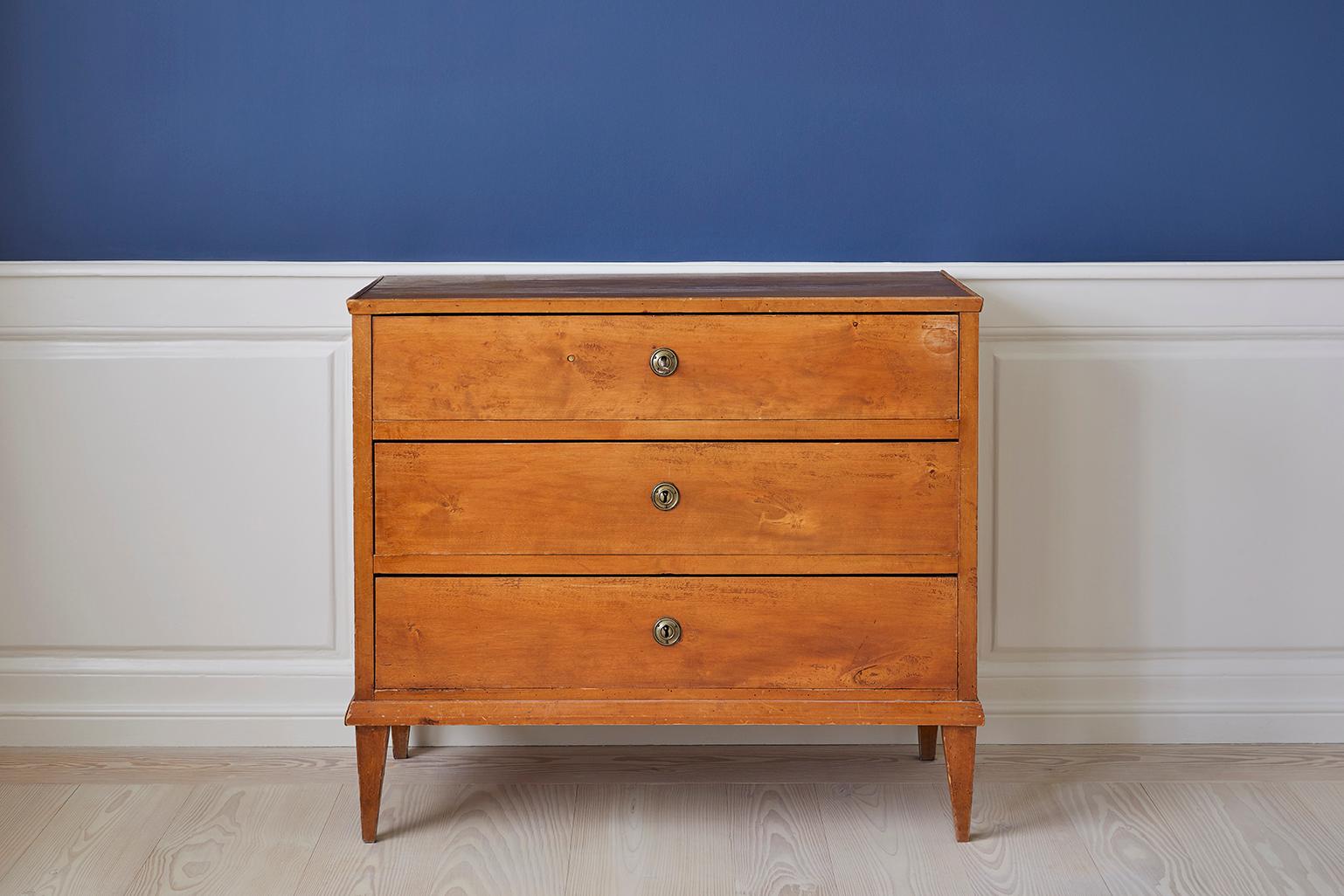 Beautiful Swedish rectangular chest of drawers veneered in birch, in the late Gustavian style. The chest has three drawers including round keyholes in brass and tapered legs. 

The vintage chest dates to back to the second half of the 19th