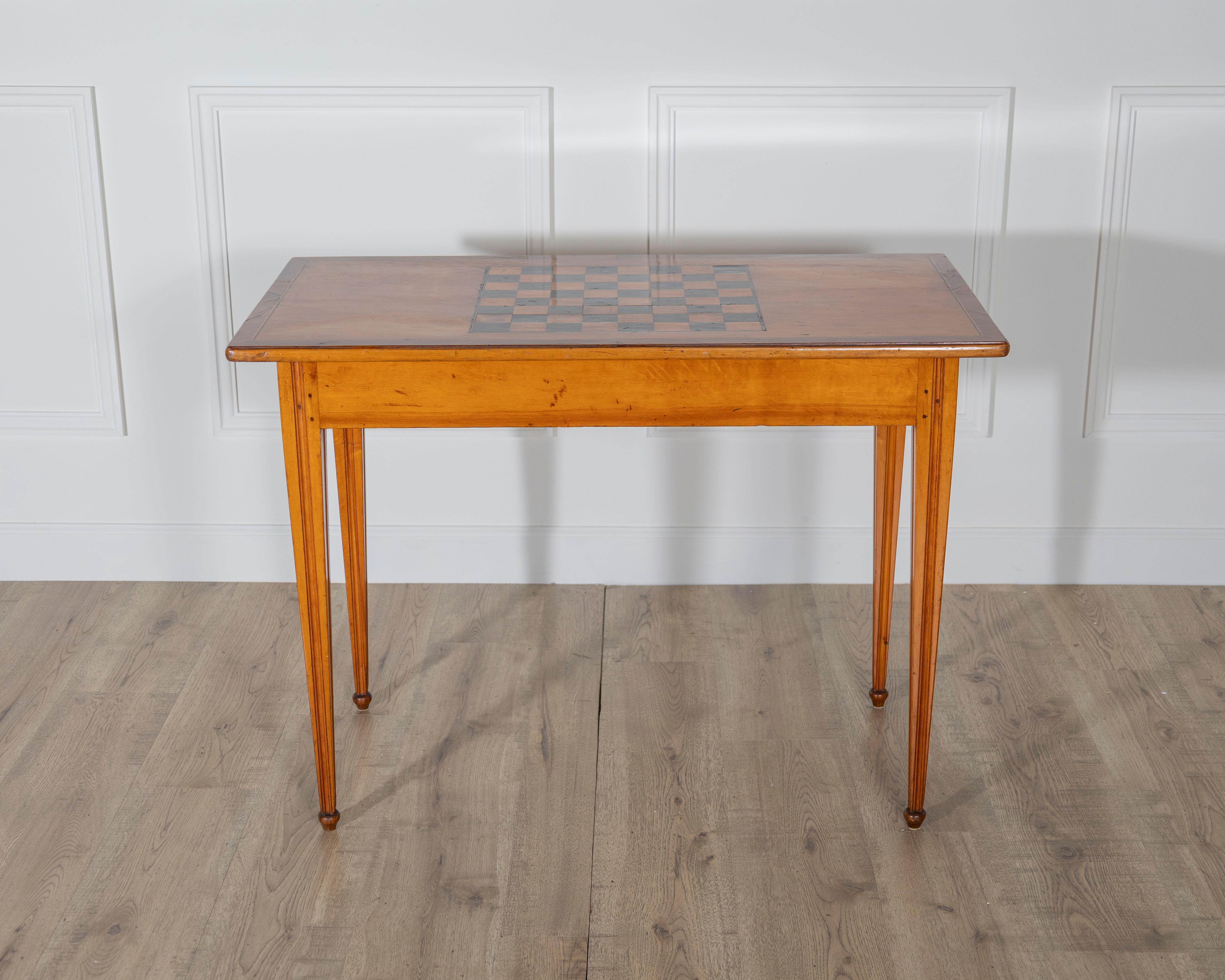 A beautiful late Gustavian game table, circa 1840, crafted in cherry with nutwood inlays, combining refined neoclassical design with playful function. The rectangular top is inlaid with a checkerboard for chess or draughts, framed by a clean edge