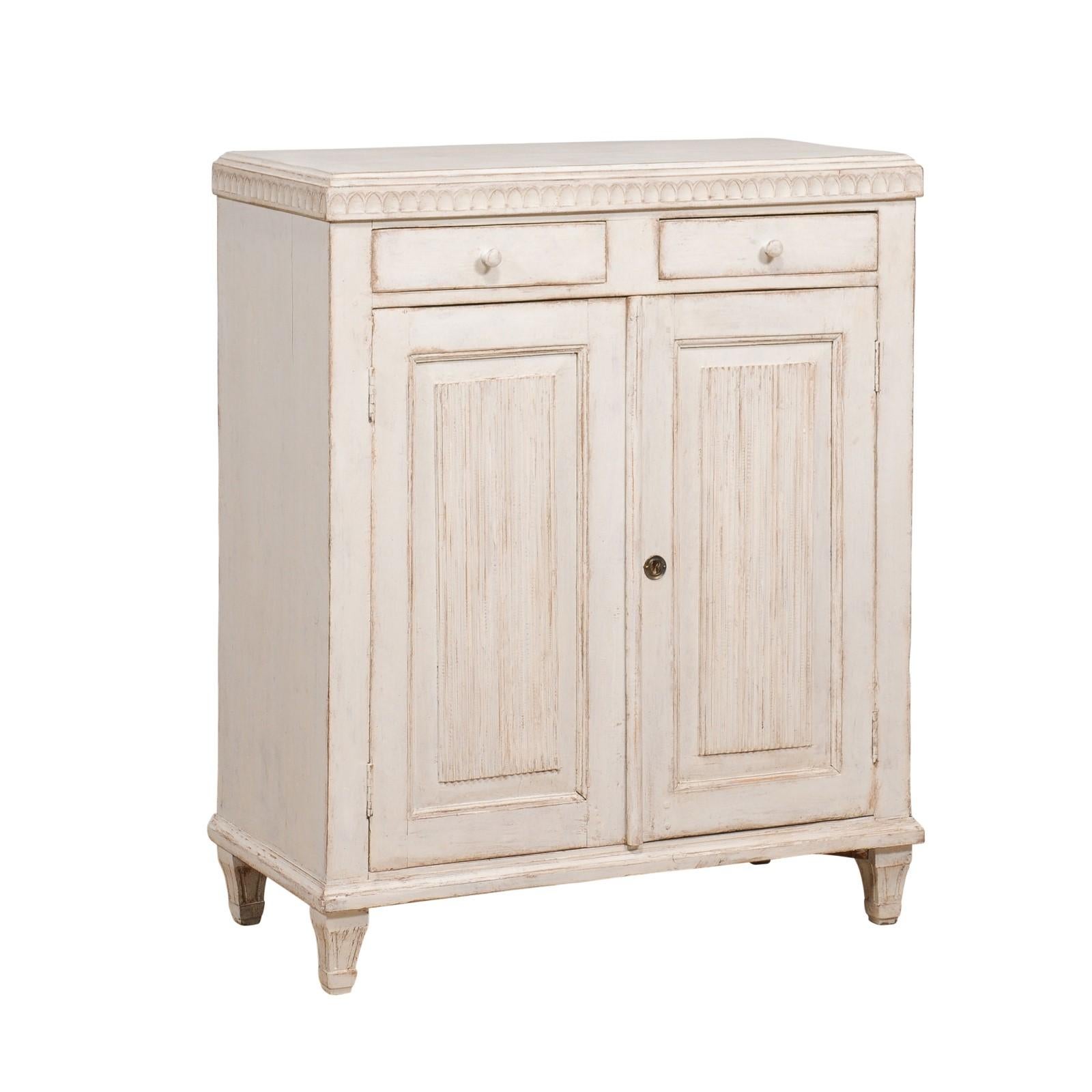 A Swedish late Gustavian period neutral light grey painted sideboard from circa 1820 with two drawers over two doors, carved molding at the top and reeded doors. Elevate your living space with the exquisite allure of this Swedish Late Gustavian