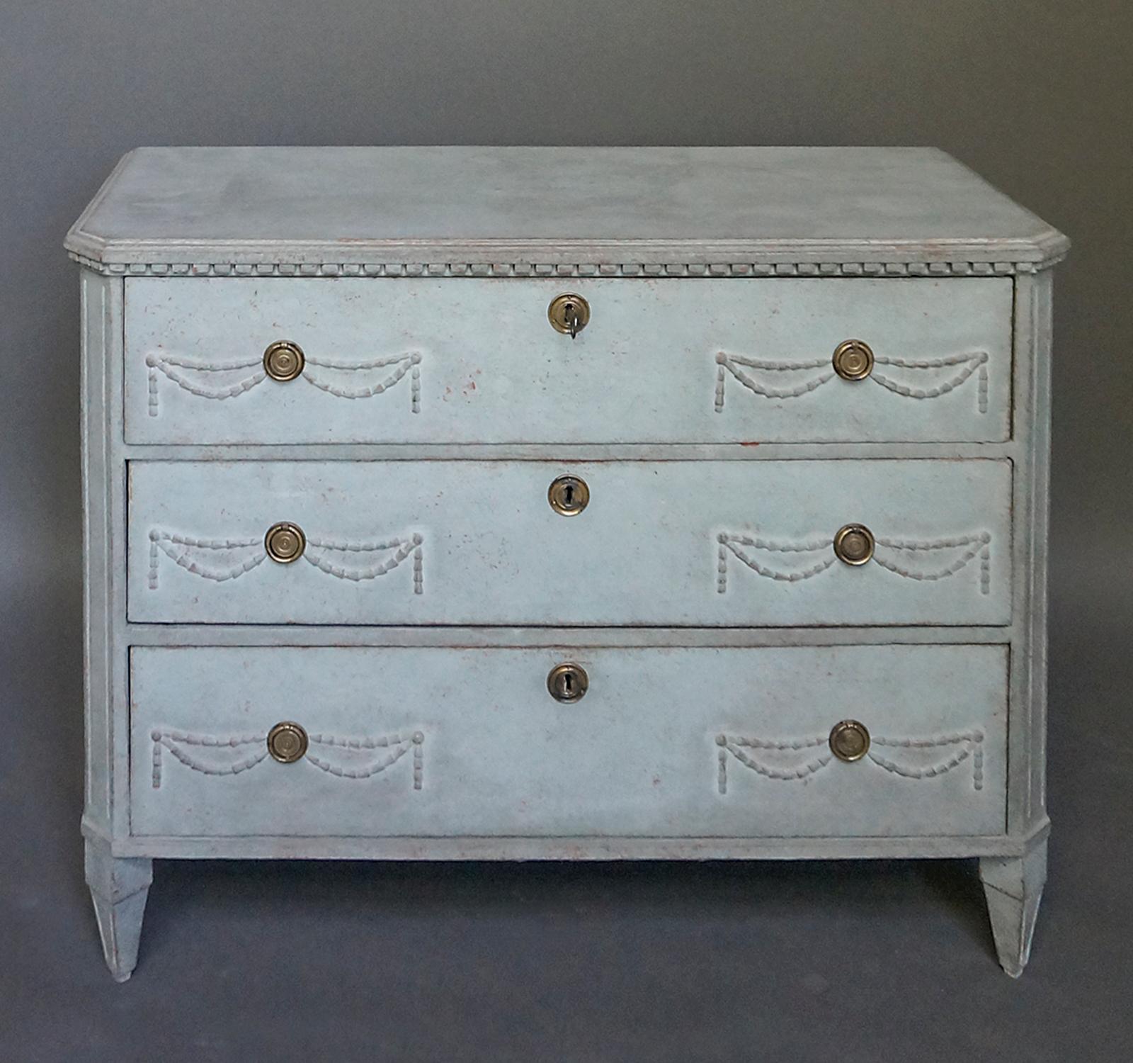 Gustavian chest of drawers, Sweden circa 1880, with applied swag detail. Shaped top with dentil molding, canted corners and tapering square feet.