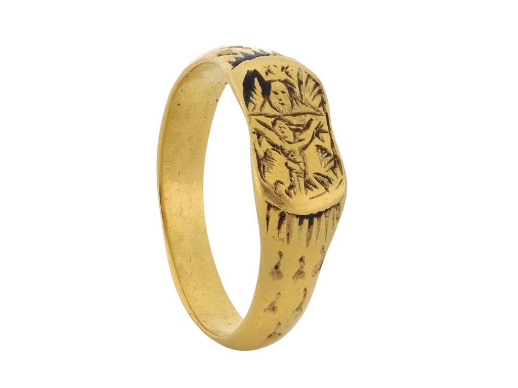 Late Medieval iconographic ring depicting the Holy Trinity. A yellow gold ring featuring a central rectangular plaque, finely engraved with the figure of Christ on the cross, underneath the bearded head of God the Father, who is flanked by the wings