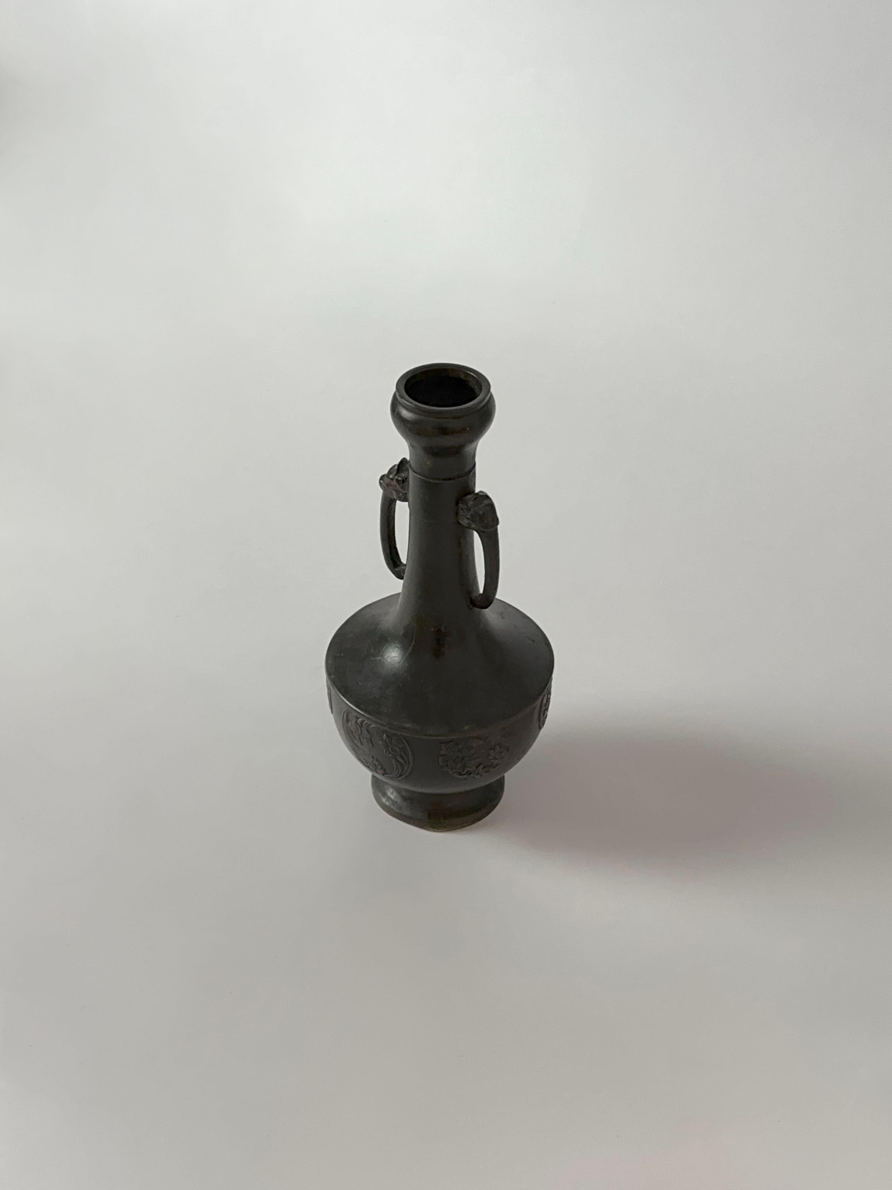 An elegant Japanese bronze bud vase dating to the late Meiji period (circa early 20th century), notable for its refined proportions and sculptural detail. The form combines a rounded, bulbous base with a narrow neck and slightly everted rim, flanked