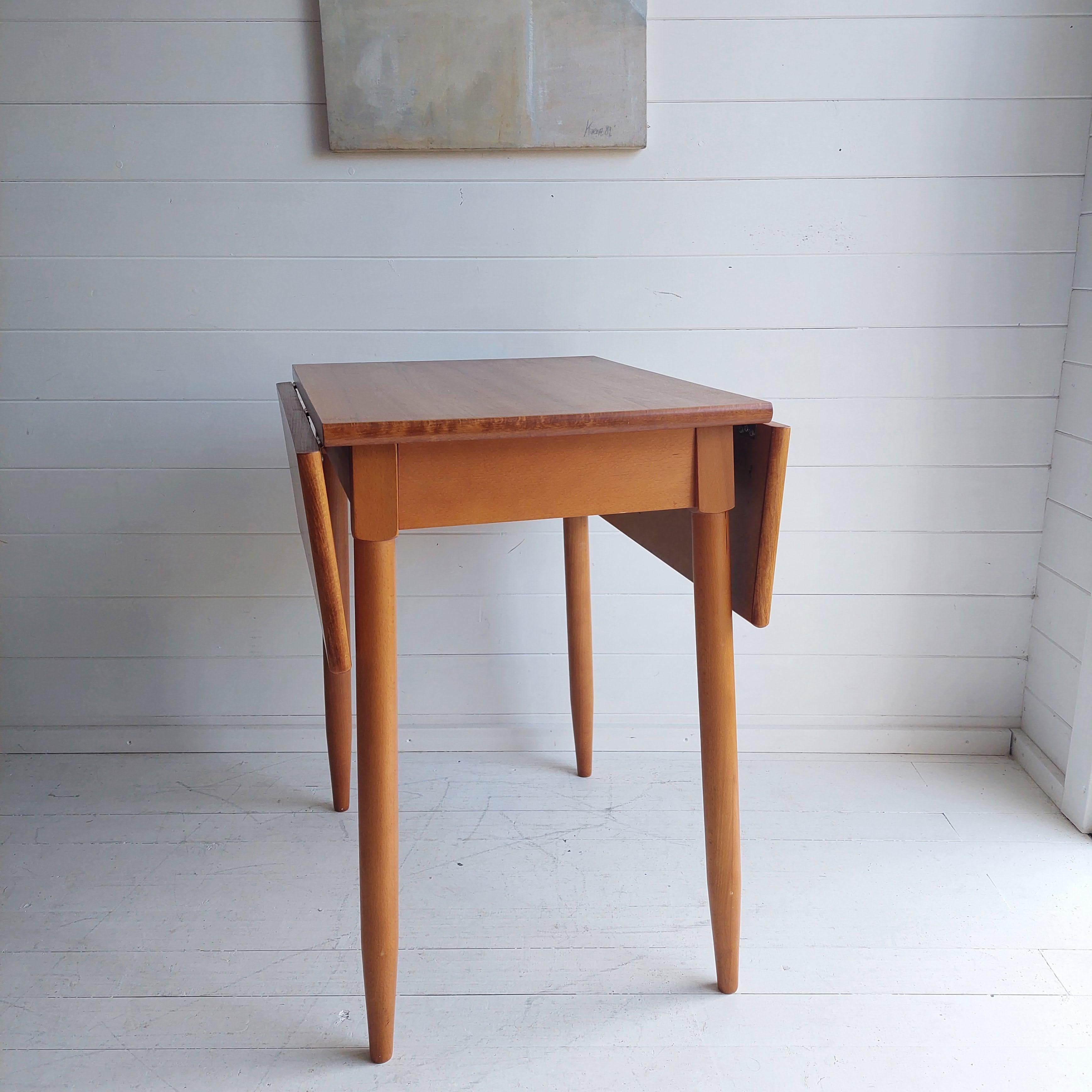 This is a small wooden drop leaf kitchen table probably dating from the 1980s. 
Vintage teak effect drop leaf table with beech frame and legs that seats 2-4 people most probably from the Czech Republic 

The table has wooden legs and the top