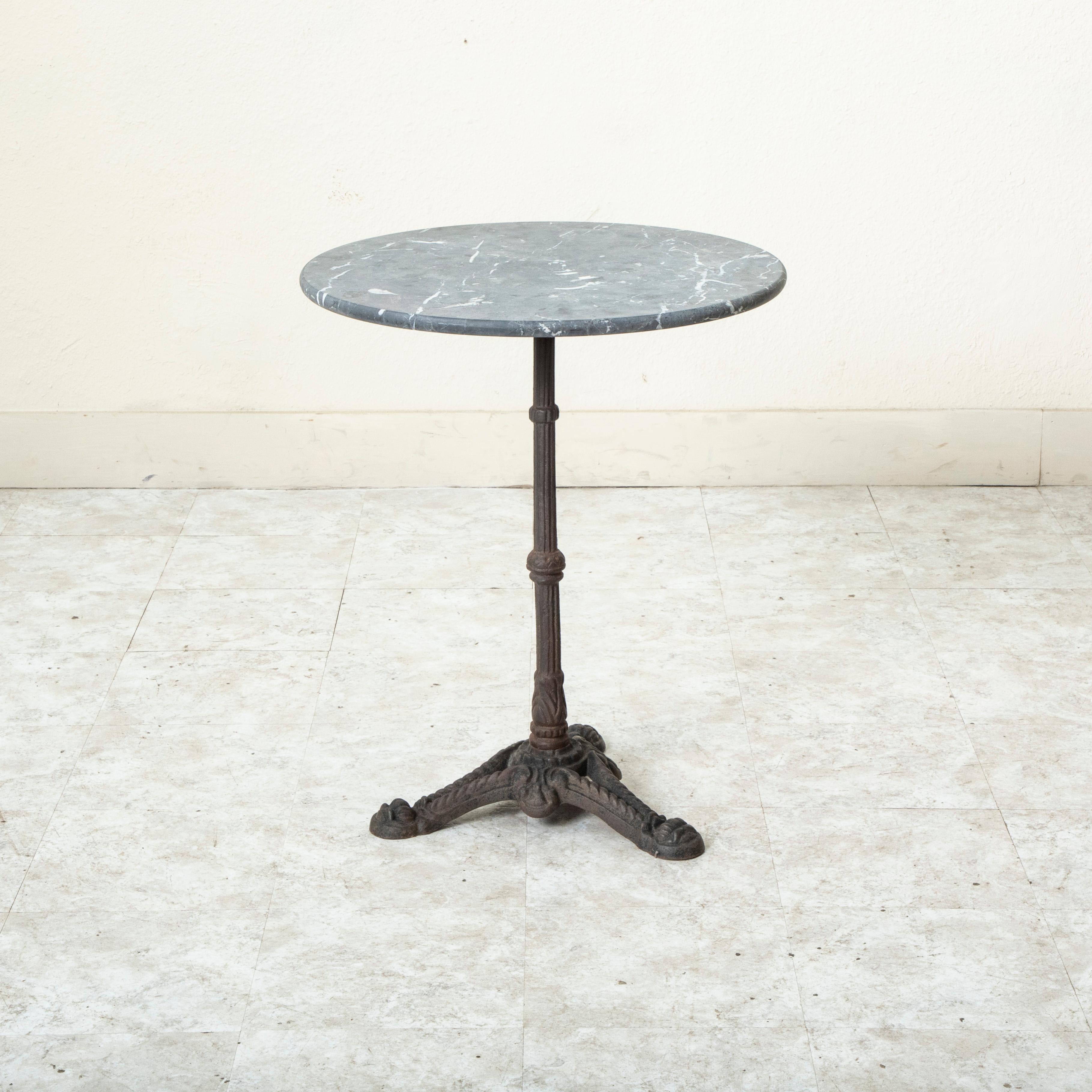 This classic French iron bistro table or cafe table from the late nineteenth century features a round grey marble top with white veining and rounded edge. The top measures 24 inches in diameter and rests on a cast iron base supported by a central