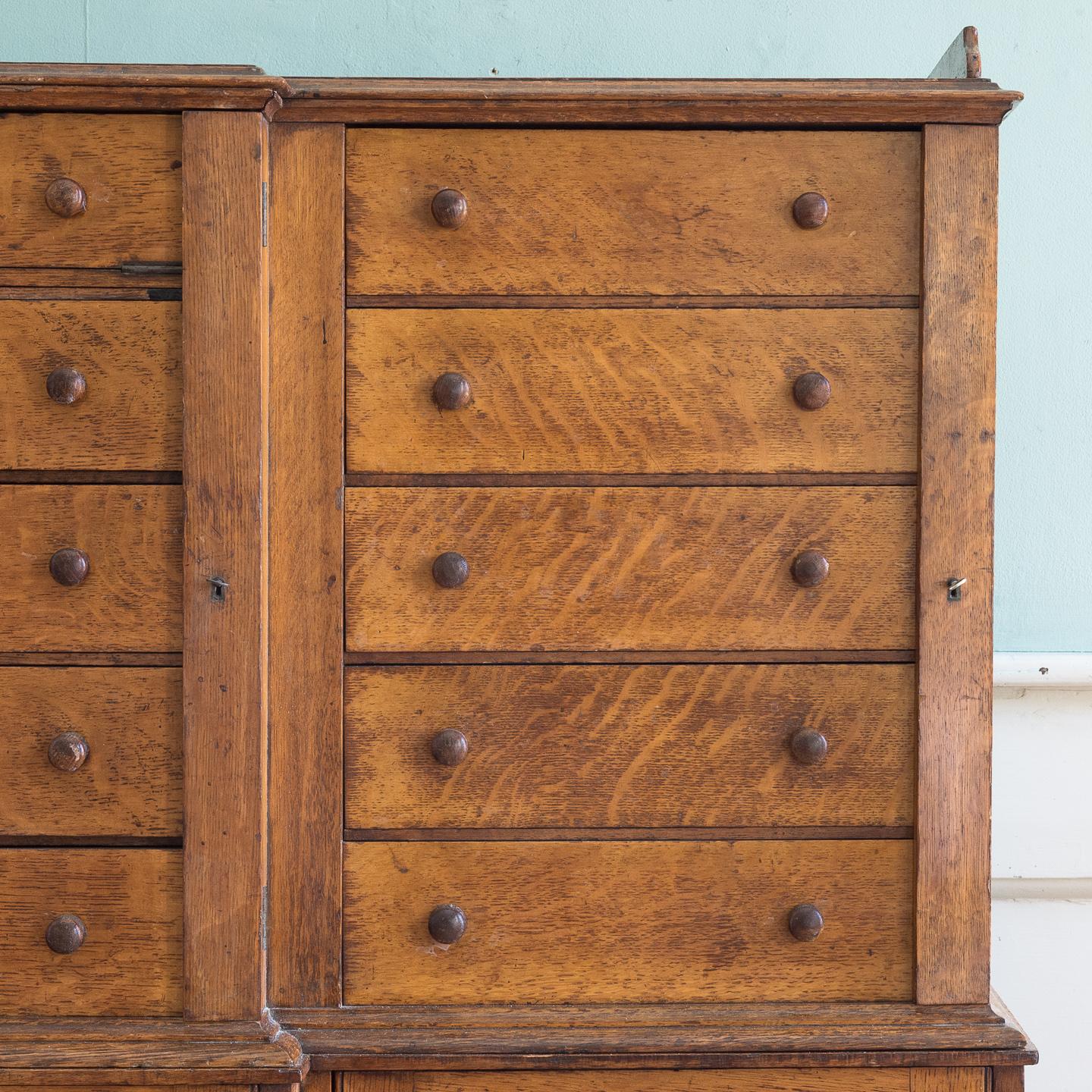 A late 19th century oak Wellington cabinet, the three-quarter galleried breakfront top above three sets of drawers flanked by lockable 'pilasters', the base with raised and fielded doors on plain plinth.