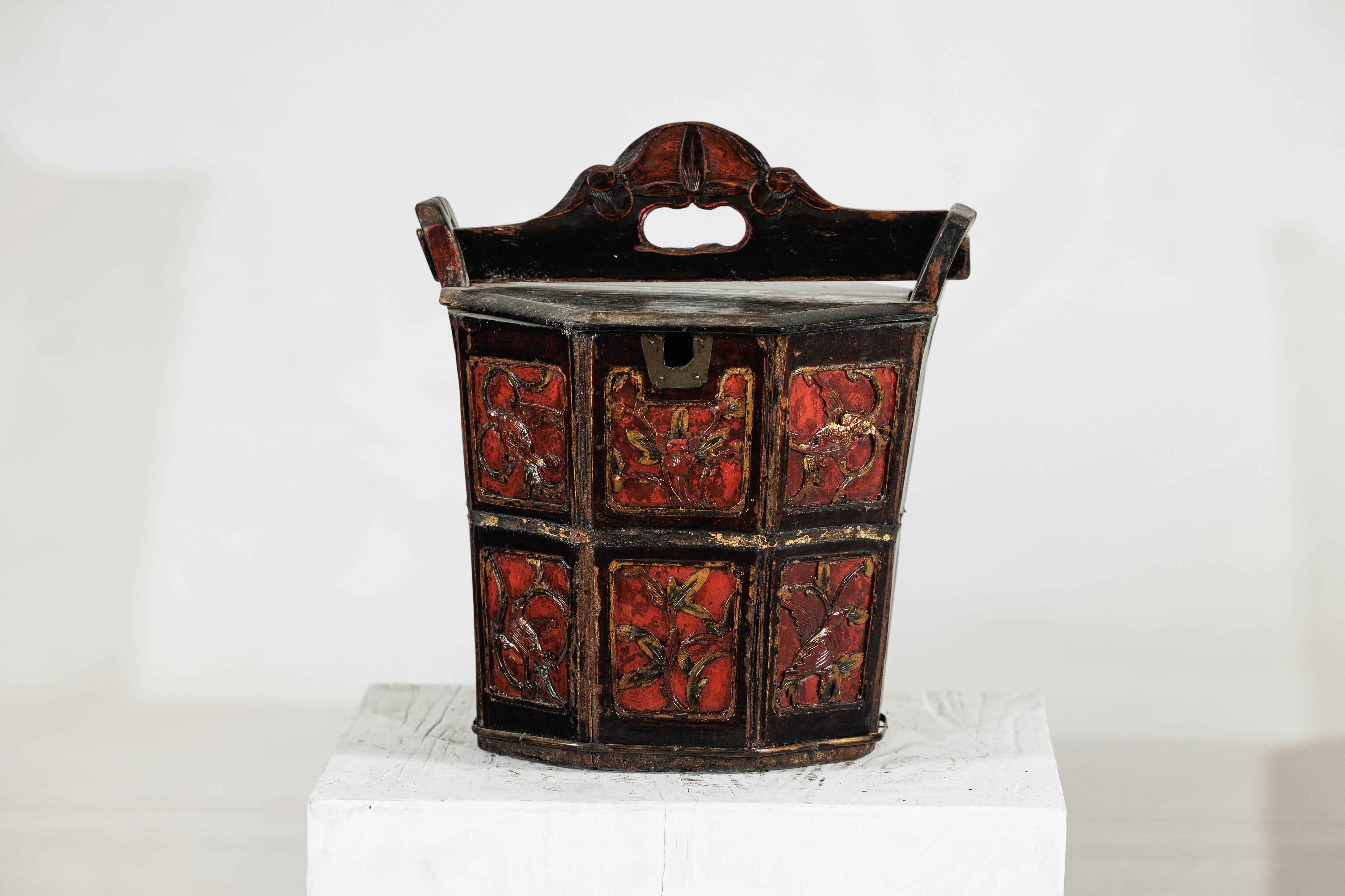 A late Qing dynasty Chinese wooden rice measure, hand-carved and richly lacquered in red and black, with traces of gilt enhancing its decorative motifs. Octagonal in form, the bucket is fitted with a lift-off lid and sturdy crest handle pierced for