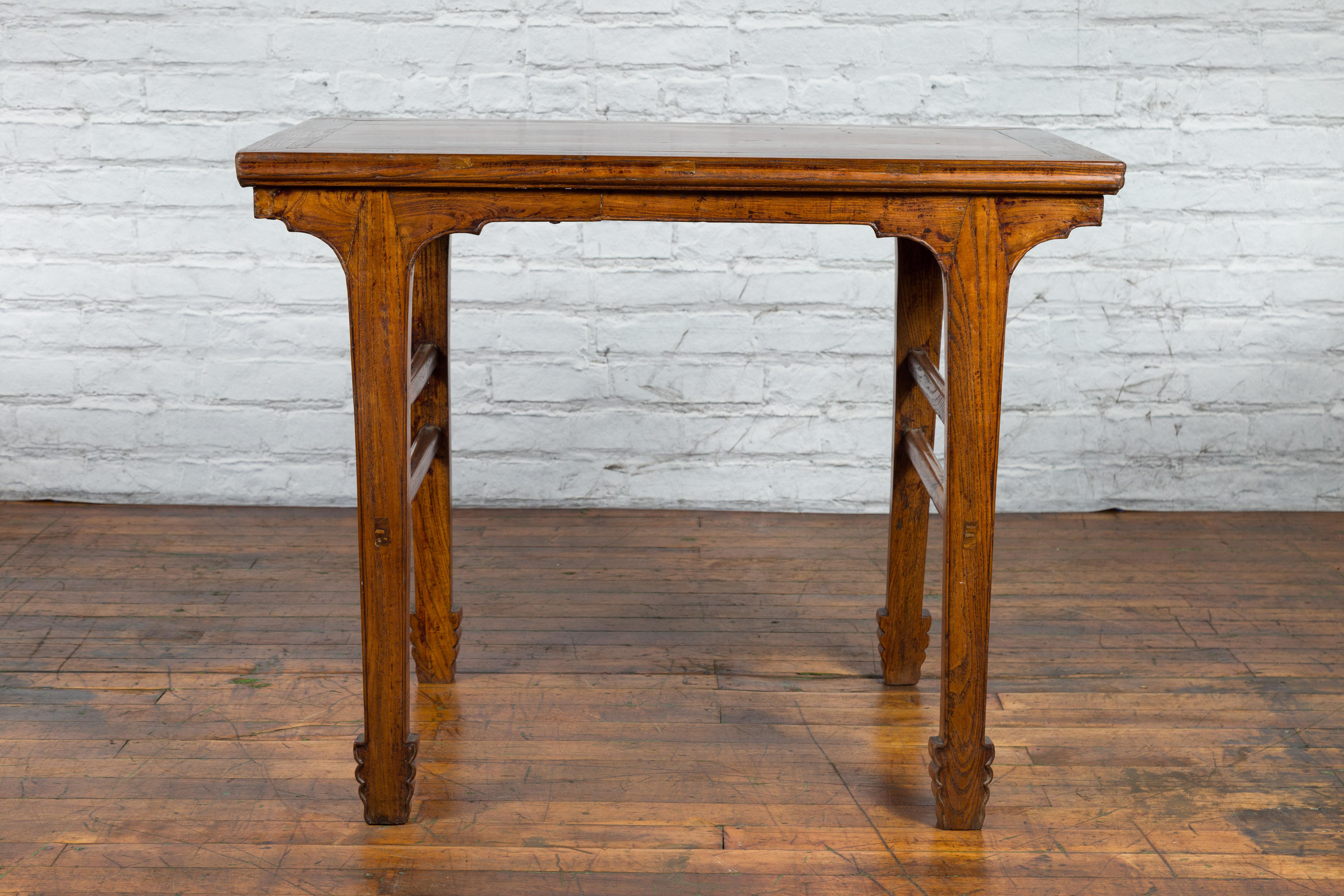 A vintage Chinese elm wood wine table from the early 20th century, with carved apron and legs, as well as double side stretchers. Created in China during the late Qing Dynasty in the early years of the 20th century, this wine table features a