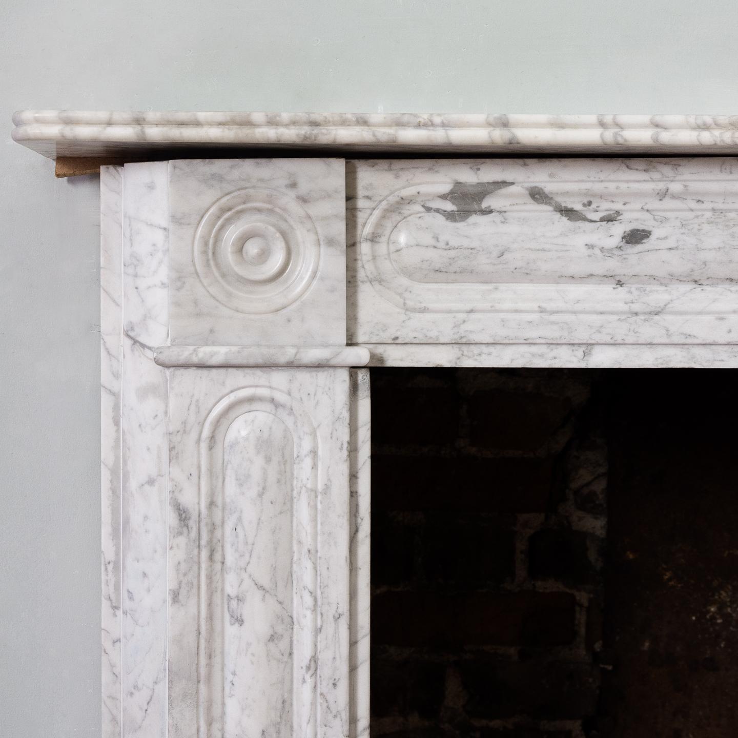 Late Regency Carrara marble bullseye fireplace, circa 1830, the reeded shelf (slightly bowed) above frieze and jambs with conforming moulded decoration.

Measures: Aperture width 90 cm x 93 cm high.
  