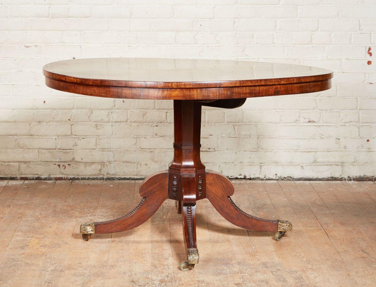 English Regency Rosewood center table with well grained top over octagonal center column having downswept legs ending in original foliate cast feet and original brass casters, circa 1830.