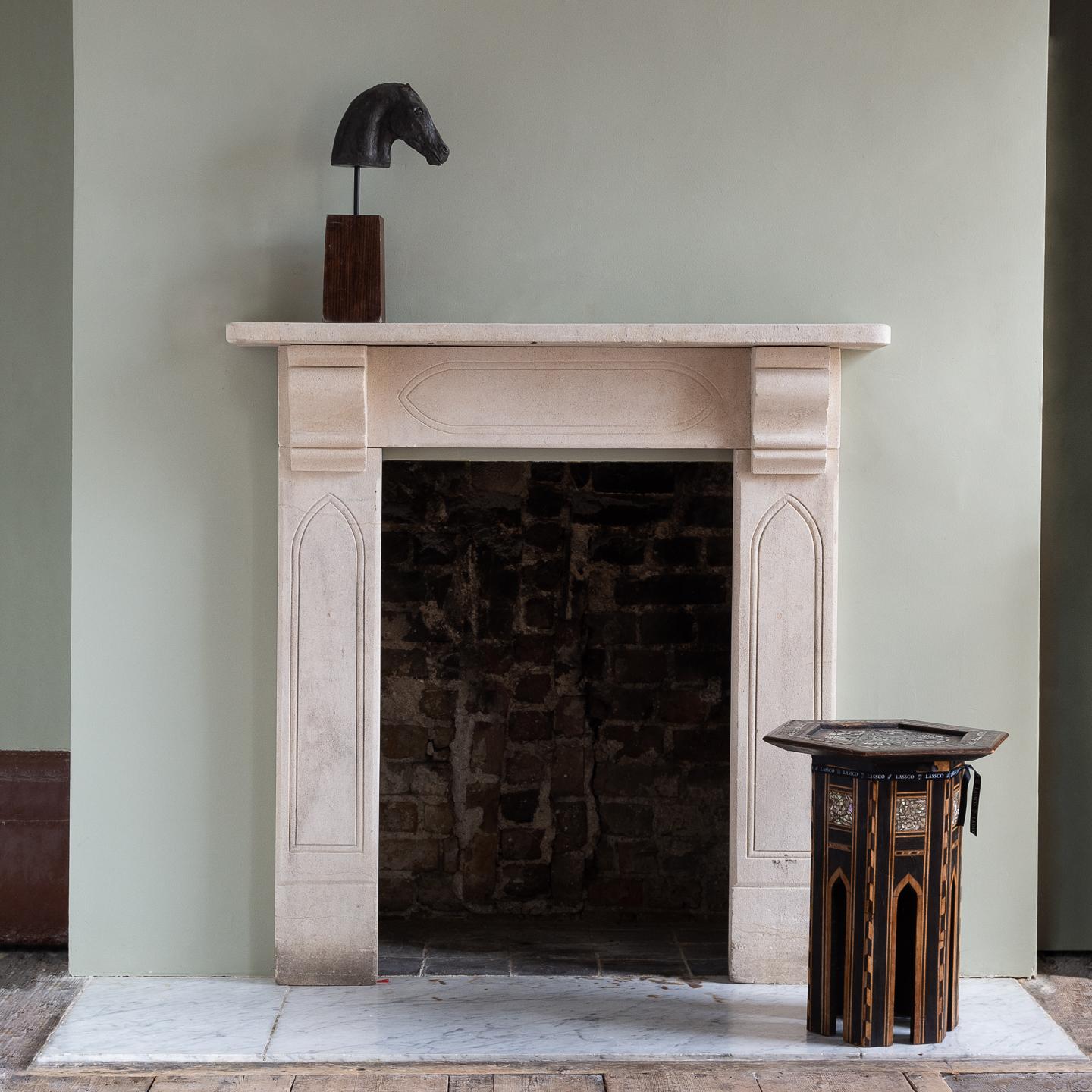 Late Regency Gothik bathstone chimneypiece, with incised lancet motif to the corbelled jambs and frieze. Measures: Opening width 61 cm x 93 cm high.