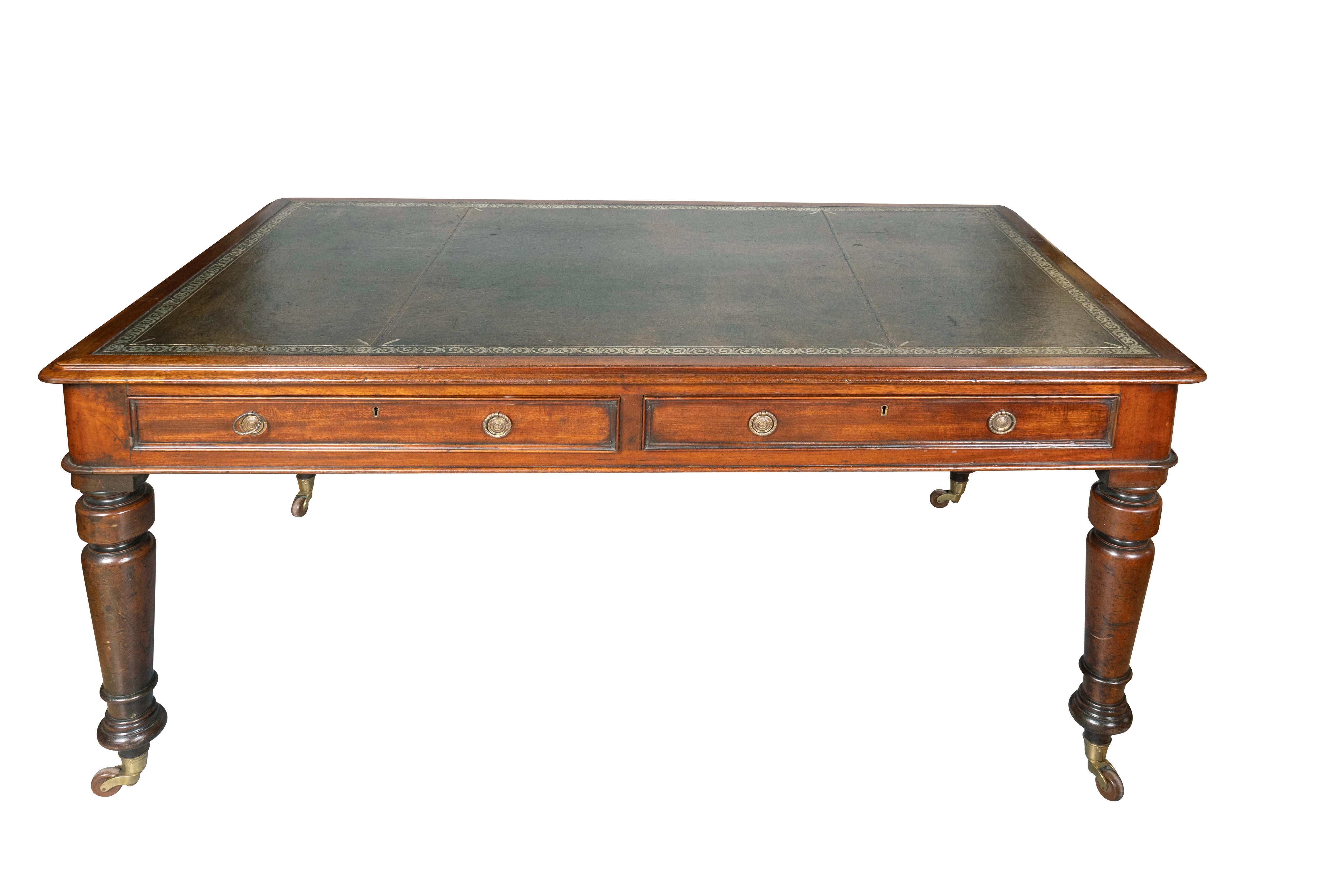 With a tooled olive green leather writing surface with wood border and molded edge over two drawers on front and back. Brass ring handles. Supported on turned tapered legs with casters.