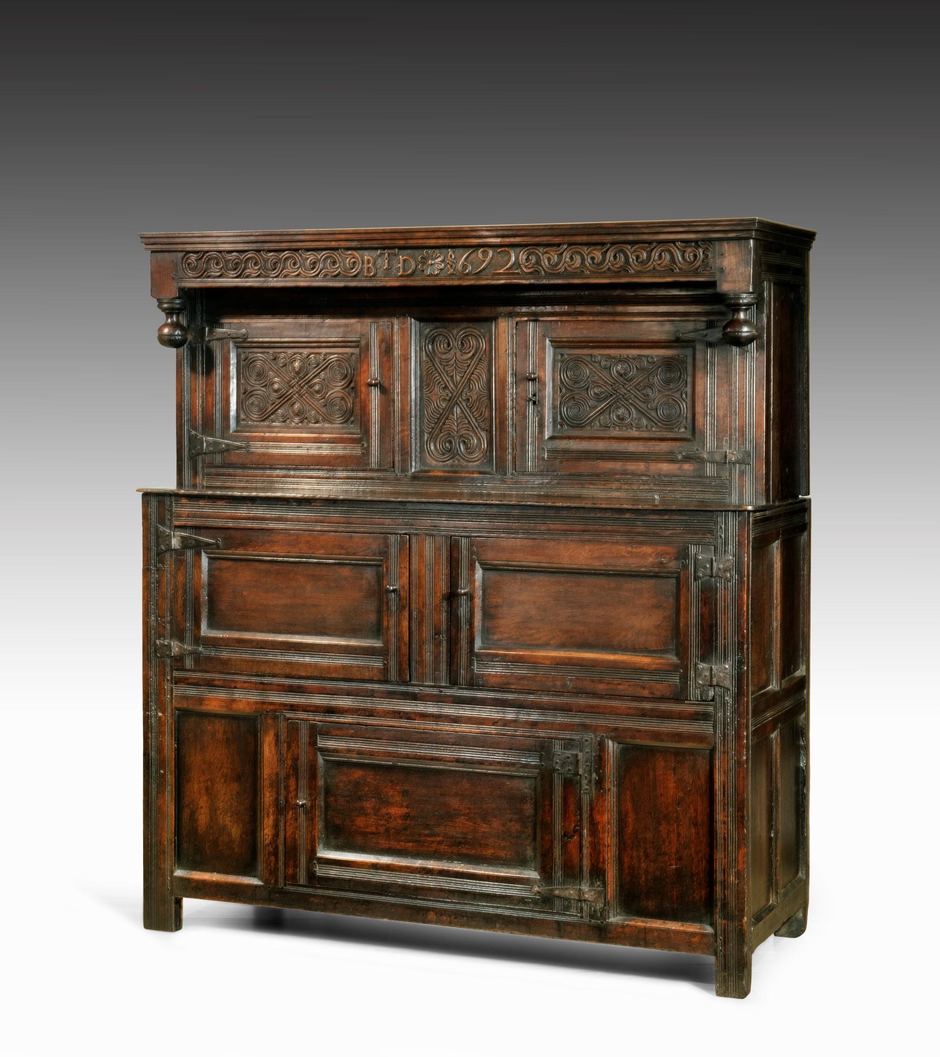 A late 17th century William and Mary period carved oak court cupboard from Westmorland. The court cupboard breaks down into two sections; the upper section has a top rail boldly carved with a scrolling motif and the date 1692 along with the initials