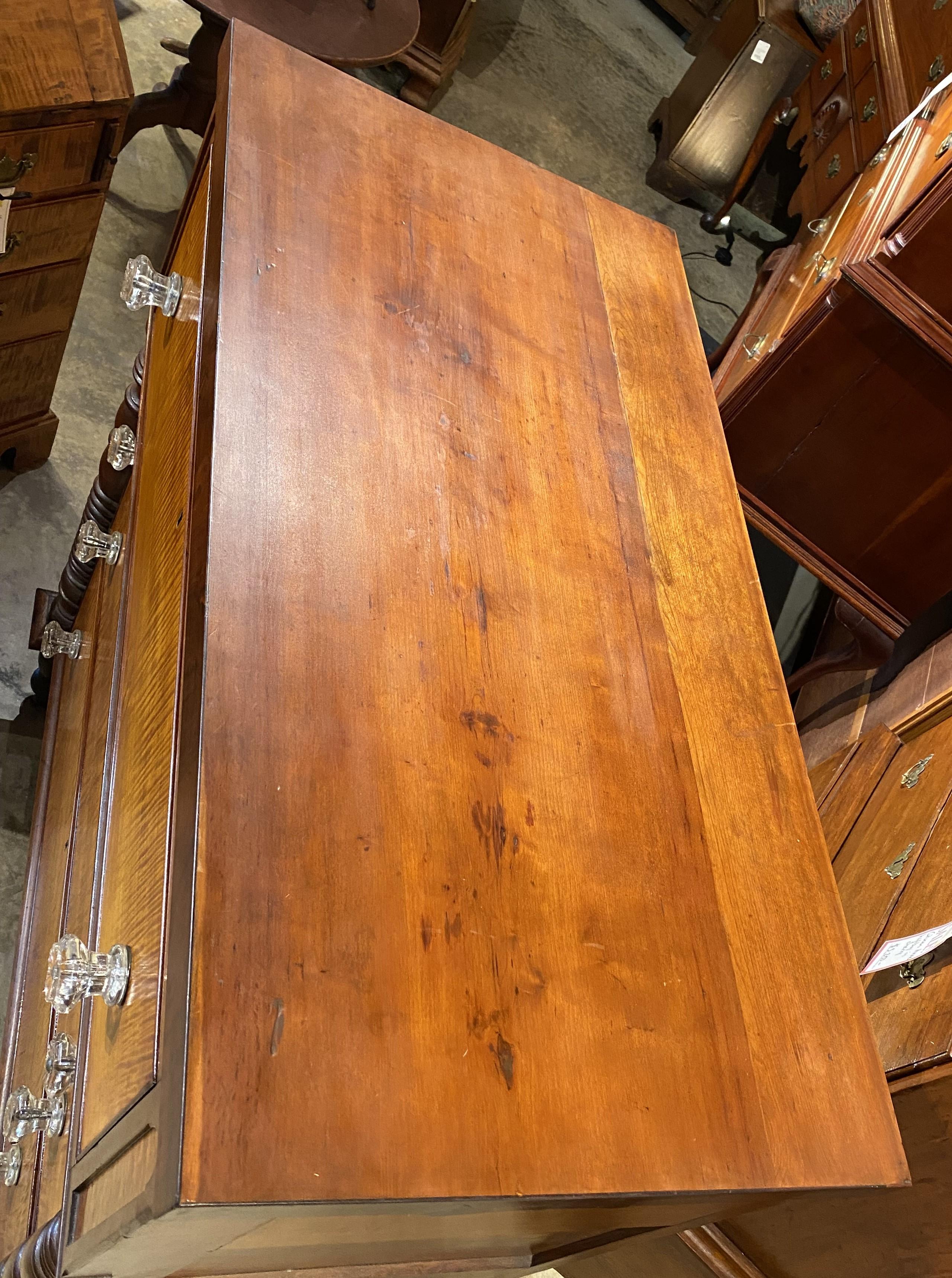 Preciosa cómoda de cuatro cajones de arce al tigre y cerezo, con tapa rectangular sobre una caja de cerezo con cuatro cajones graduados, cada uno de ellos con frentes chapados en arce al tigre y pomos de cristal, flanqueados por dos paneles