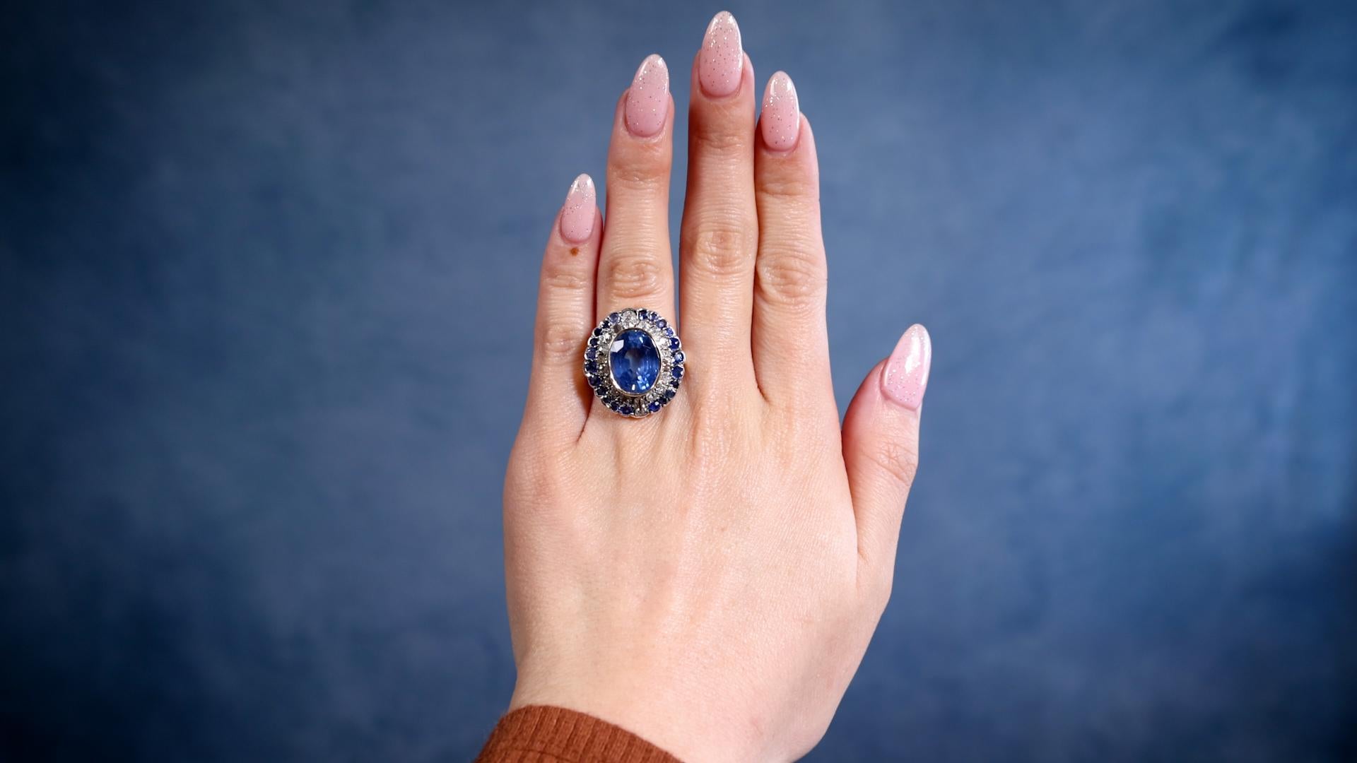One Late Victorian 10.07 Carat Sapphire and Diamond Silver 10k White Gold Cluster Ring. Featuring one oval mixed cut sapphire weighing 10.07 carats. Accented by 18 mixed cut diamonds with a total weight of approximately 0.70 carats, graded