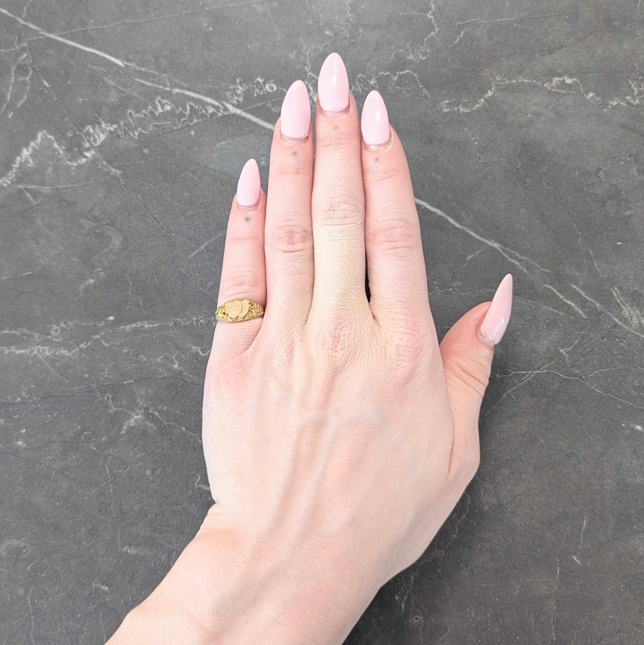 Centering two intersecting yellow gold heart forms with flat faces
With a recessed surround accented by raised grapevine motifs
Depicted with grapes, foliate, gold nugget and rose gold vines
Accented by crosshatch texture engraving
Stamped for 14