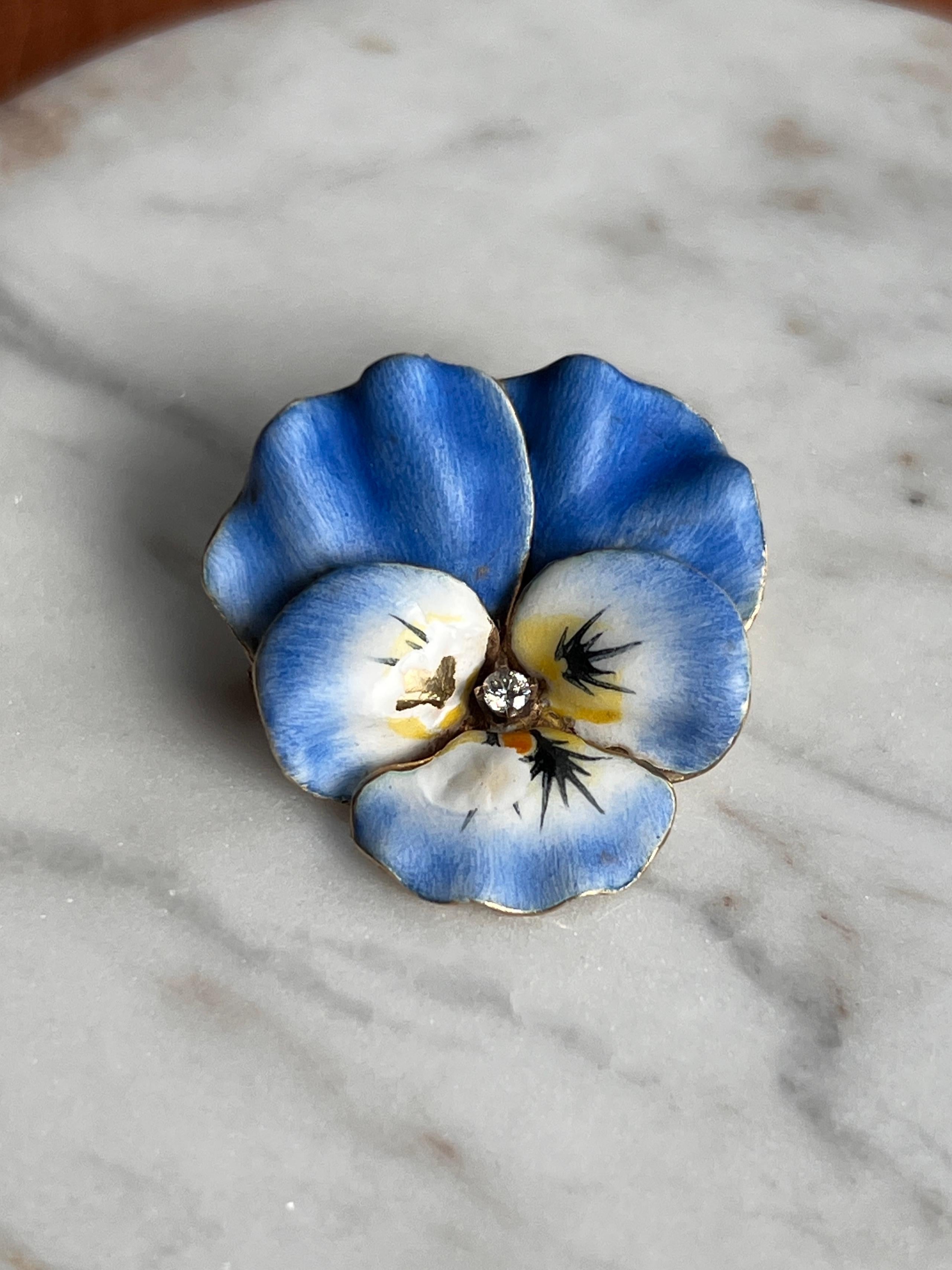 This enchanting 1890s pin is crafted in 14 karat yellow gold and depicts a delicate pansy motif in blue, white, black, and yellow enamel. A single 2mm round paste stone—lead glass cut to sparkle like a gemstone—sits at the center. Paste was widely