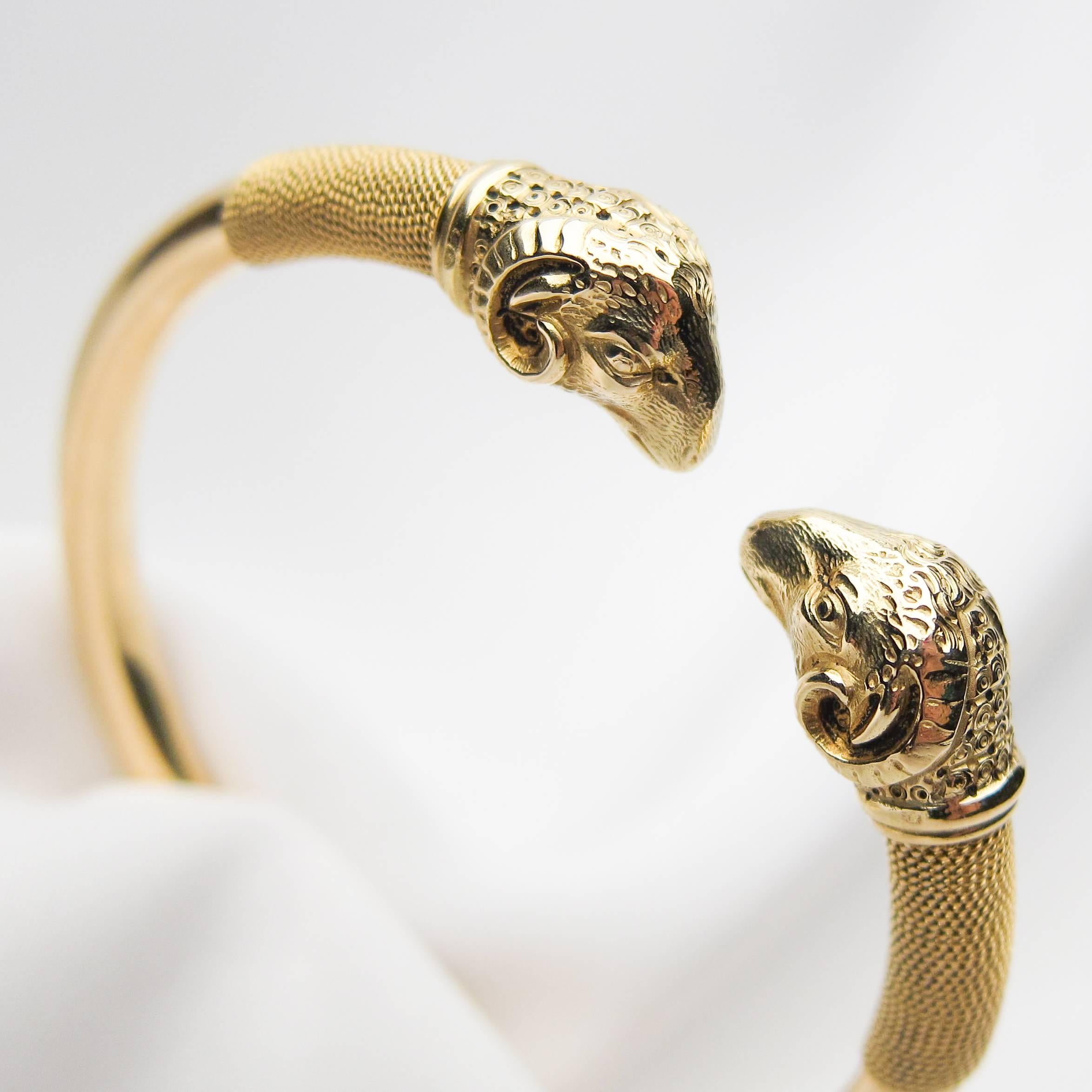 Circa 1900. This mesmerizing Late Victorian Era 18KT gold bangle features two beautifully detailed ram's heads facing one another from each end of the cuff-style bracelet. Delicate gold rope accents add a lovely textural note against the smooth