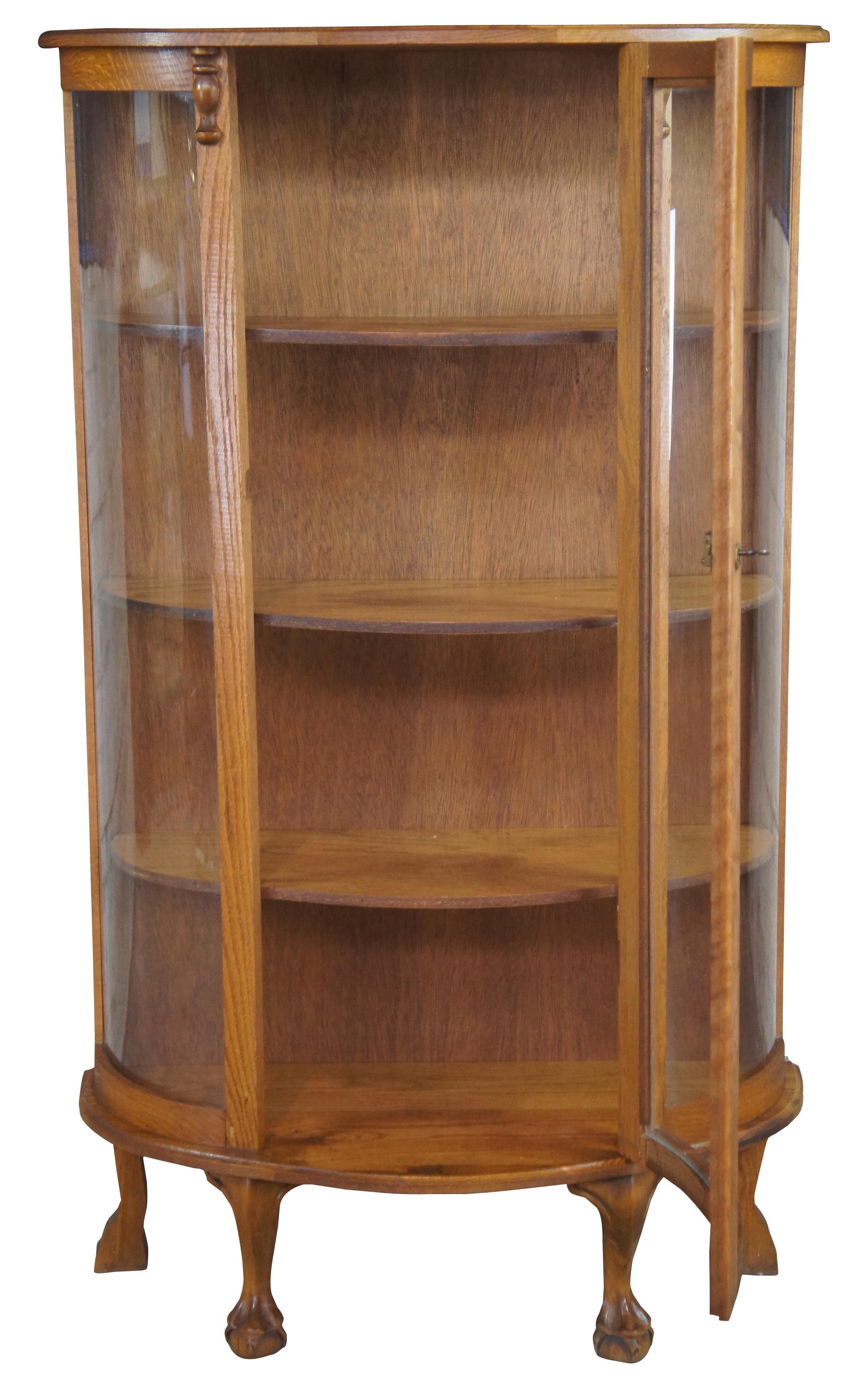 Early 20th century oak bowfront curio or display cabinet. Features a demiulune form with three shelves over ball and claw feet.
 