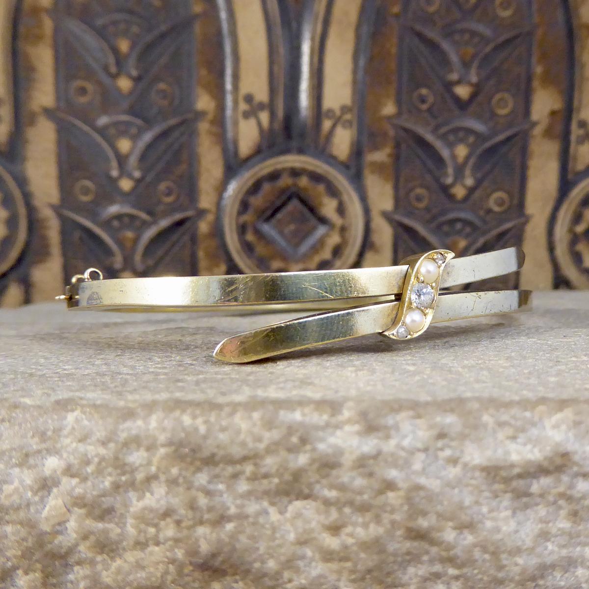 This beautiful antique bracelet was hand crafted in the Late Victorian era from 15ct Yellow gold. The bracelet clasp is safe and secure on the side of the bangle and the top has a twist aesthetic with a Diamond and Seed Pearl set banner.

Condition: