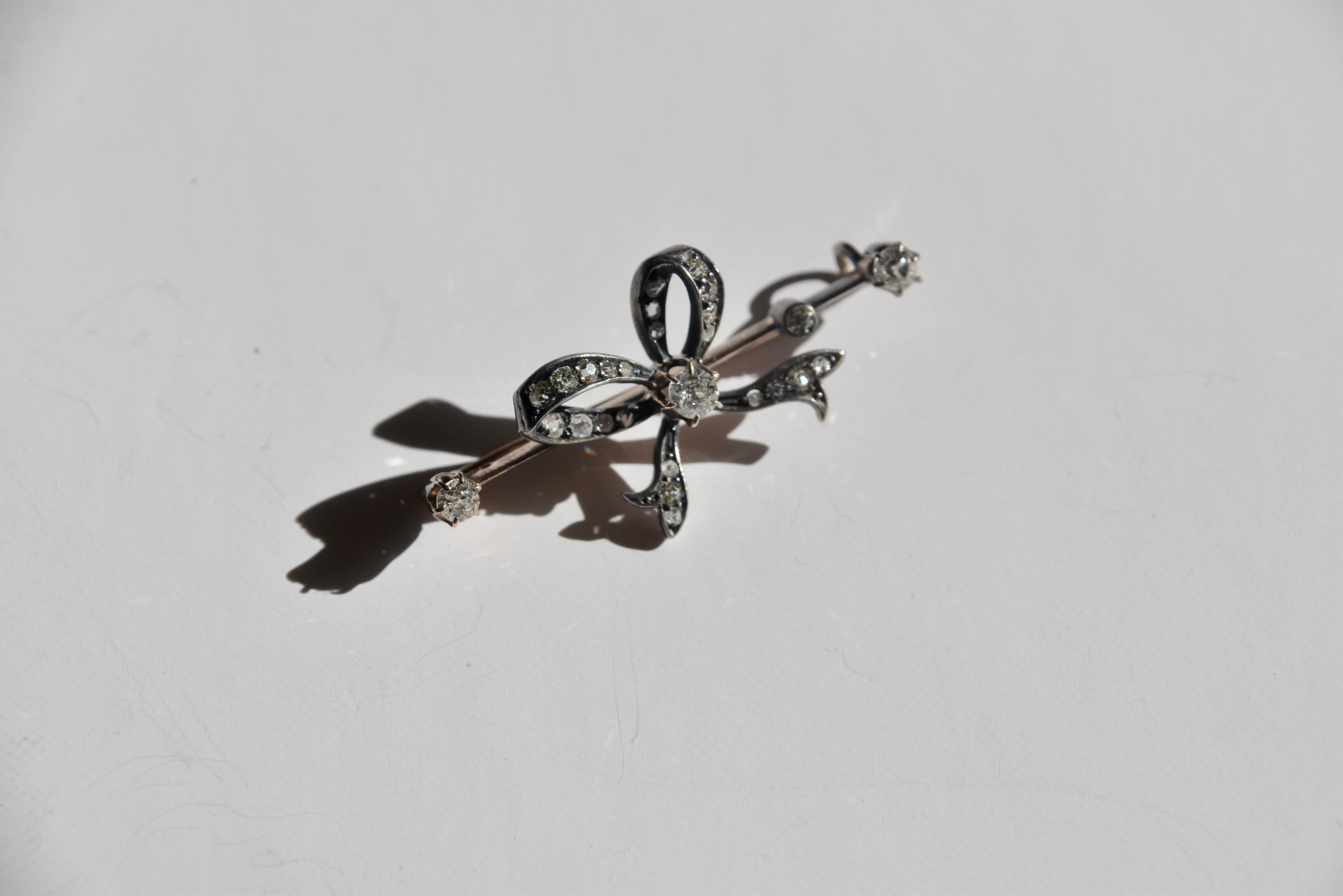 A late Victorian diamond set bow bar brooch, circa 1890, with and old European cut diamond, claw set to the centre of the bow. The loops and tails are grain set with rows of Swiss-cut, rose-cut and old eight-cut diamonds. A blade edge bar, rub set