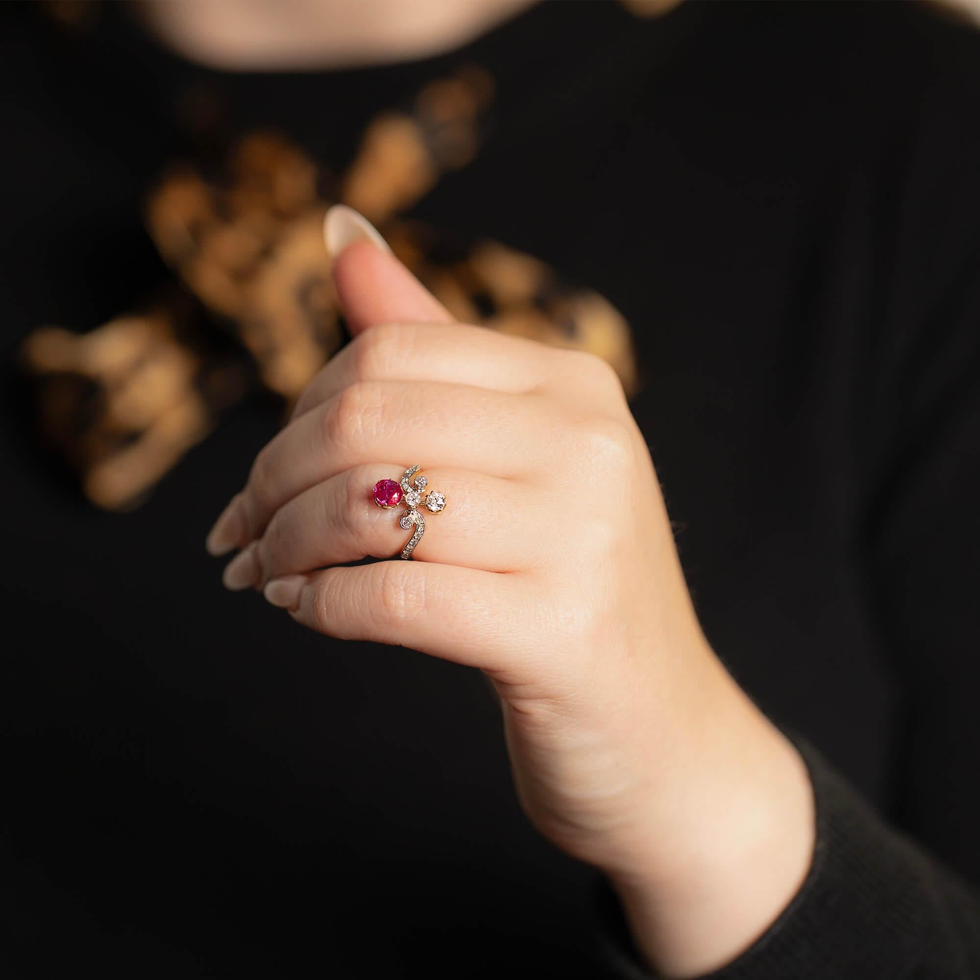 This late Victorian ring features a two mille-grained diamond set swirls that flow to to three central bezel set diamonds. A stunning oval ruby and early European cut diamond are set in the north-south positions to allow this ring to sit perfectly