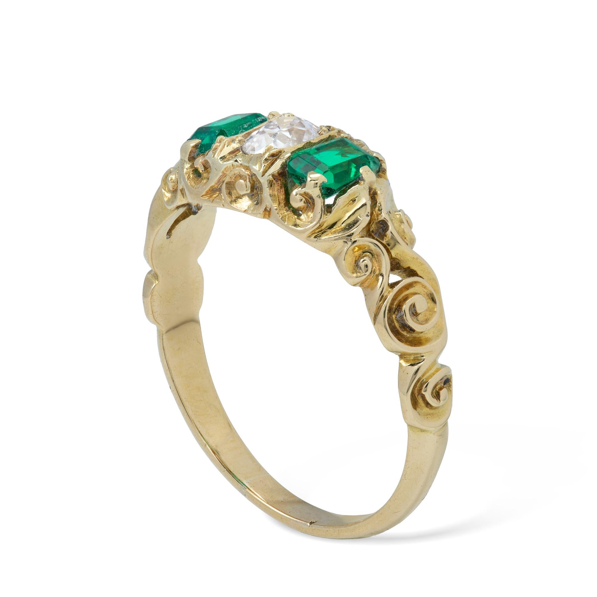 A late Victorian emerald and diamond three stone ring, the oval-cut diamond weighing approximately 0.30 carats set between two emerald-cut emeralds, weighing approximately a total of 0.60 carats, all se in a yellow gold carved mount with scroll