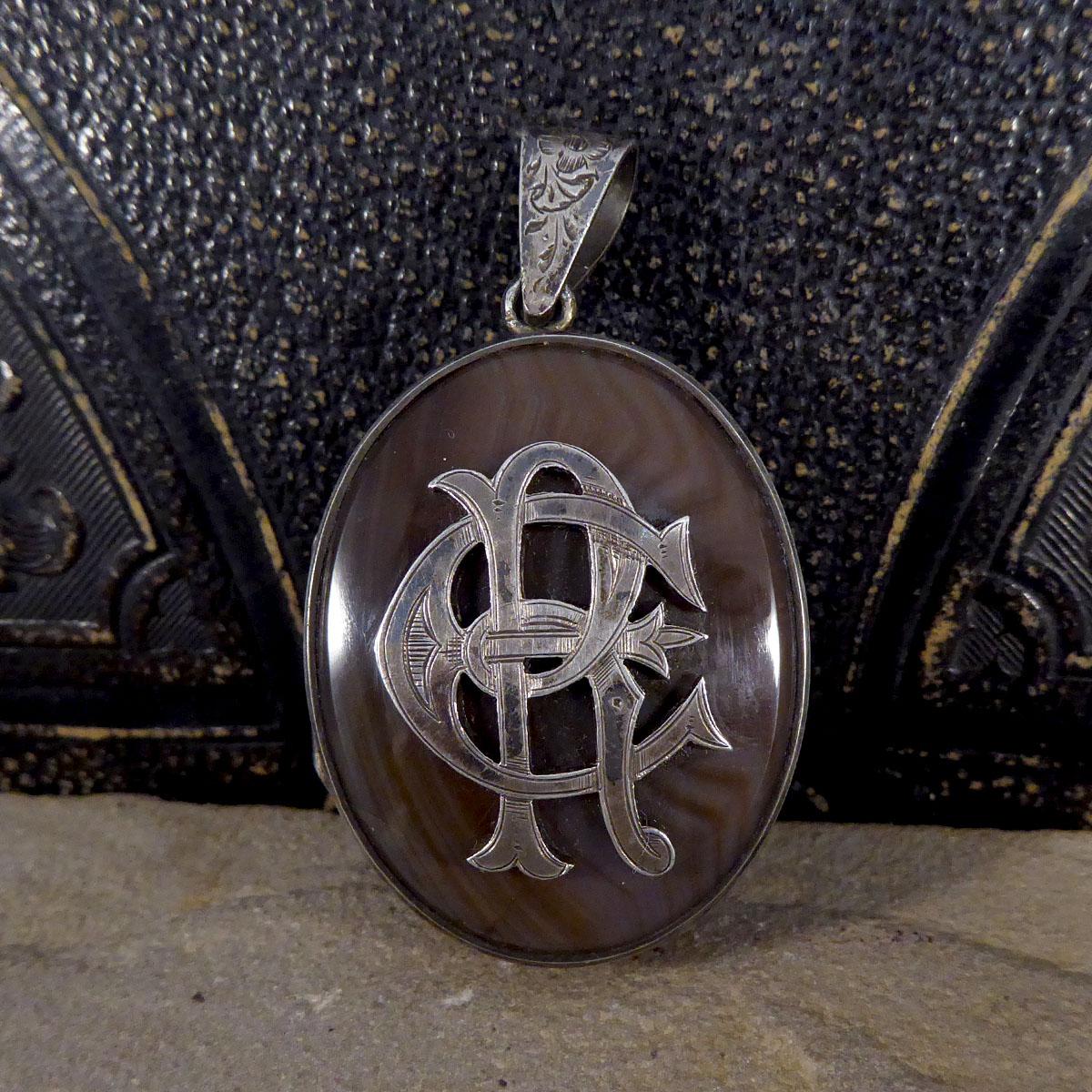 This large detailed antique Late Victorian pendant featuring engraved detail along the sides and bail. This locket has been crafted with silver and would look great on a silver chain, it has an Agate front and back with the initials E and R adorned