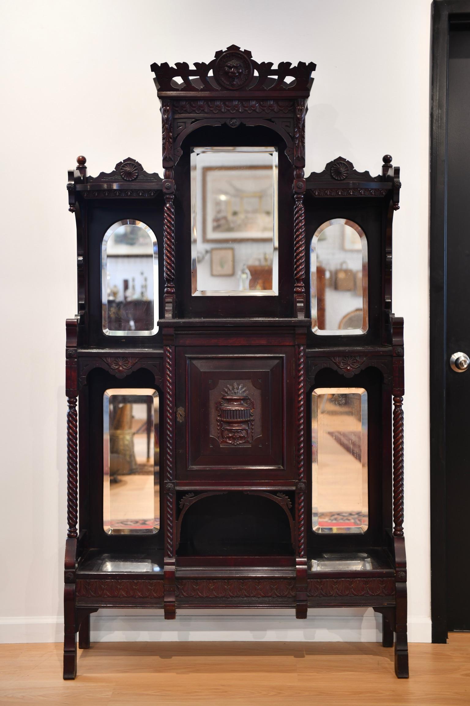 Late 19th century Victorian mahogany entryway etagere, with lion face pediment over spiral posts, open shelves, and five beveled mirrored back panels and a carved center panel cabinet. Some scratching to surfaces, pictured. Dimensions: 77