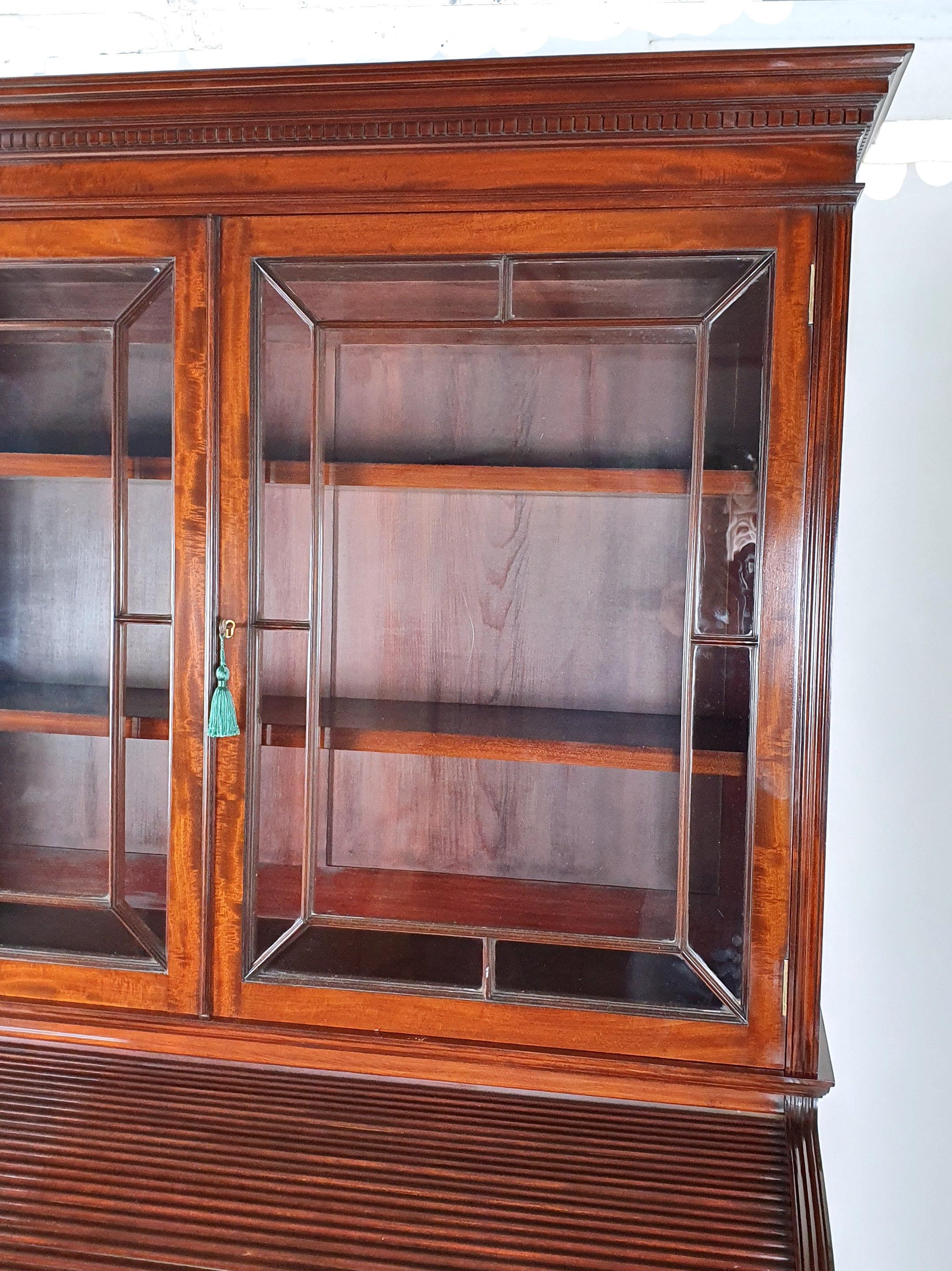 This very handsome and superb quality Victorian figured mahogany cylinder bookcase supported on a pedestal base. The 2 door glazed top features 2 adjustable shelves with the original lock and key. The bottom section features a pedestal desk with a