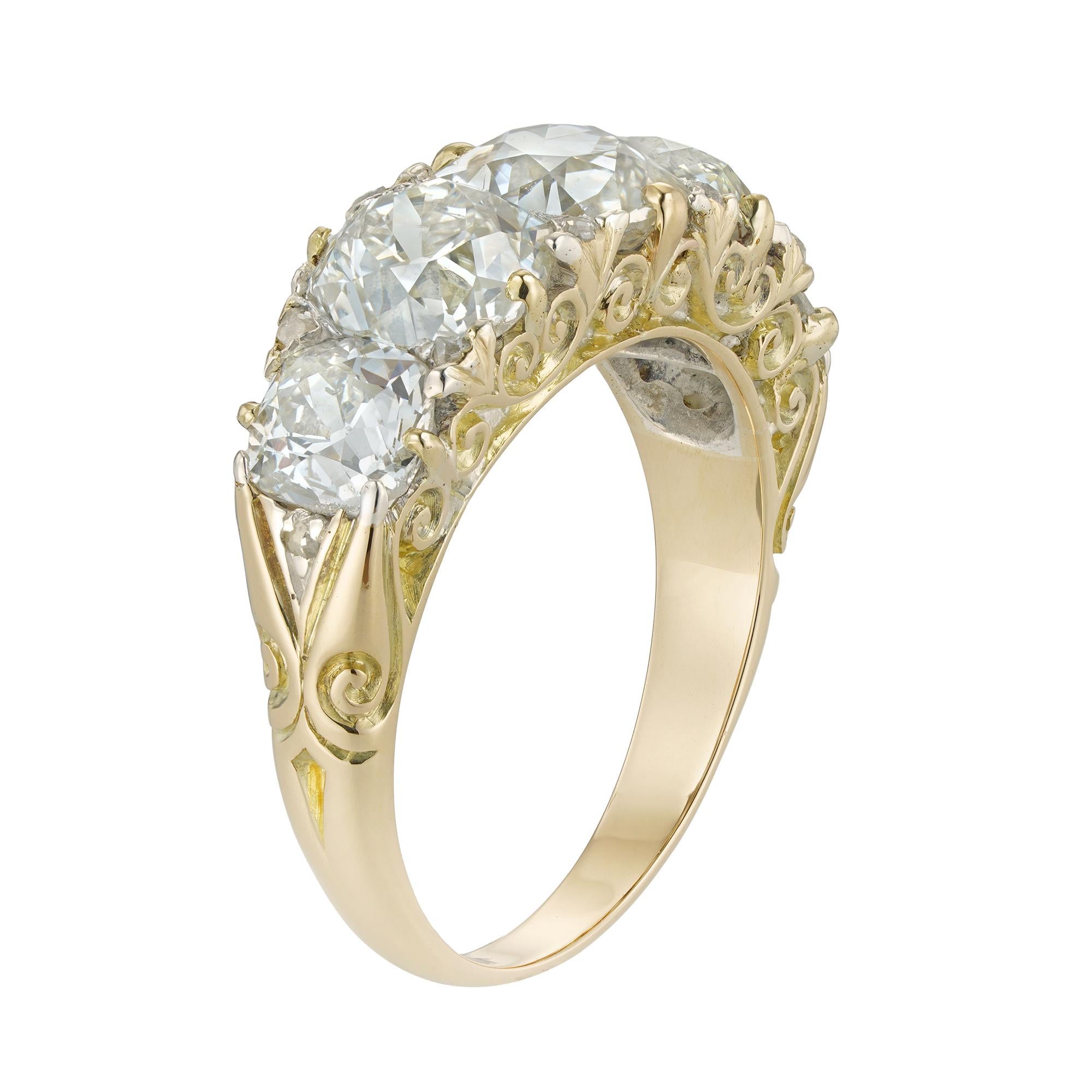 A late Victorian five-stone diamond ring, the five old-mine-cut diamonds graduating from the centre and estimated to weigh a total of 5.6 carats, all claw-set with rose-cut diamonds in-between, to a yellow gold mount with scroll engraved sides and