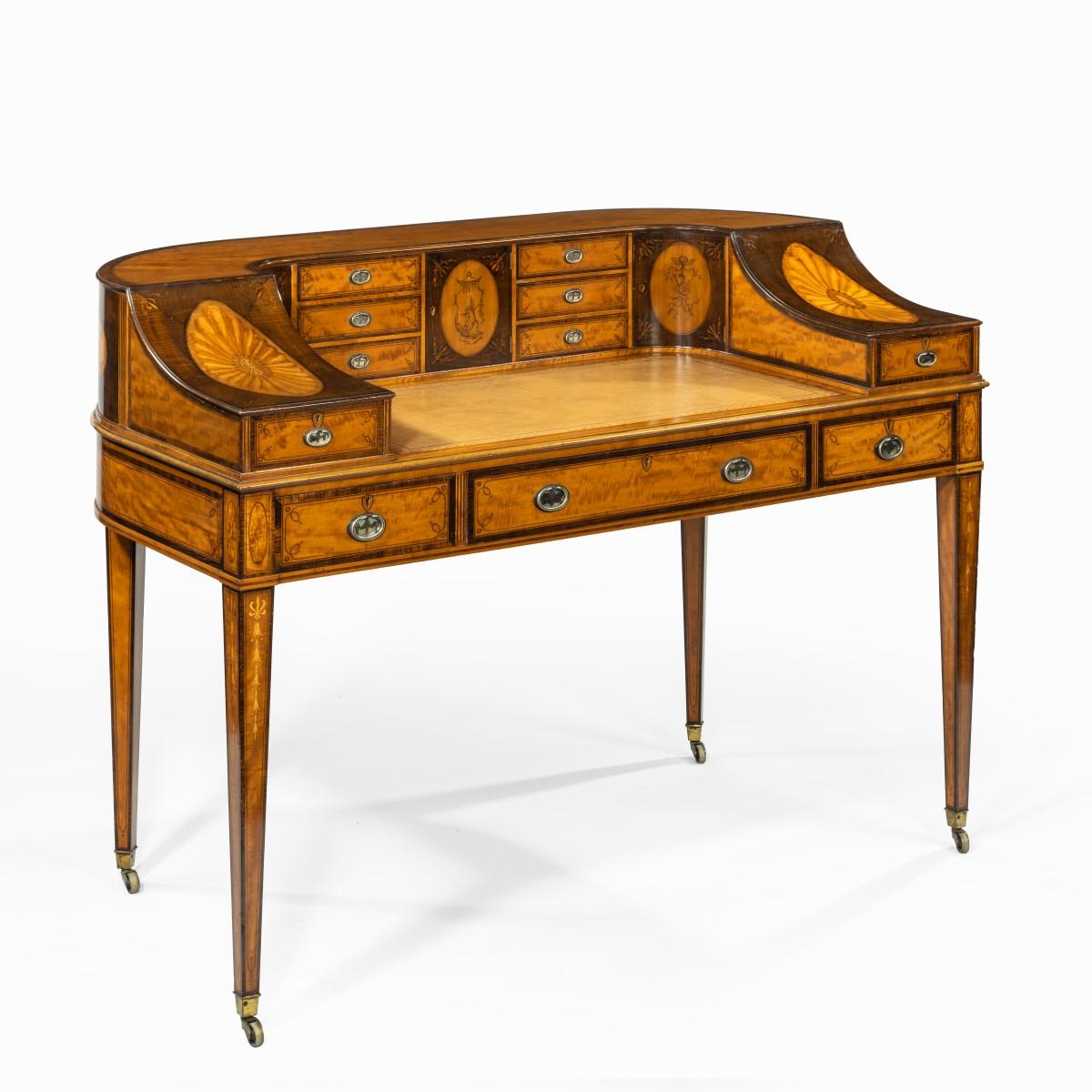 A late Victorian freestanding satinwood Carlton House desk, the curved rectangular top with the typical arrangement of six small drawers and a central cupboard around three sides, enclosing a leathered writing surface, sloping downwards to the